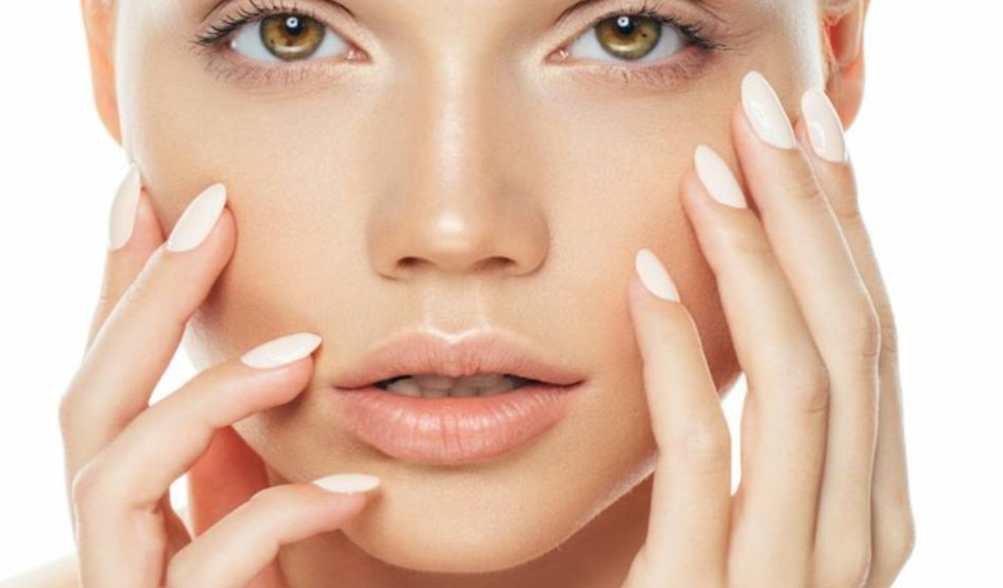 Close-up of a woman’s face with fingers gently touching her cheek in a professional beauty pose, promoting discounted microneedling services for new models in exchange for before-and-after skincare photos.