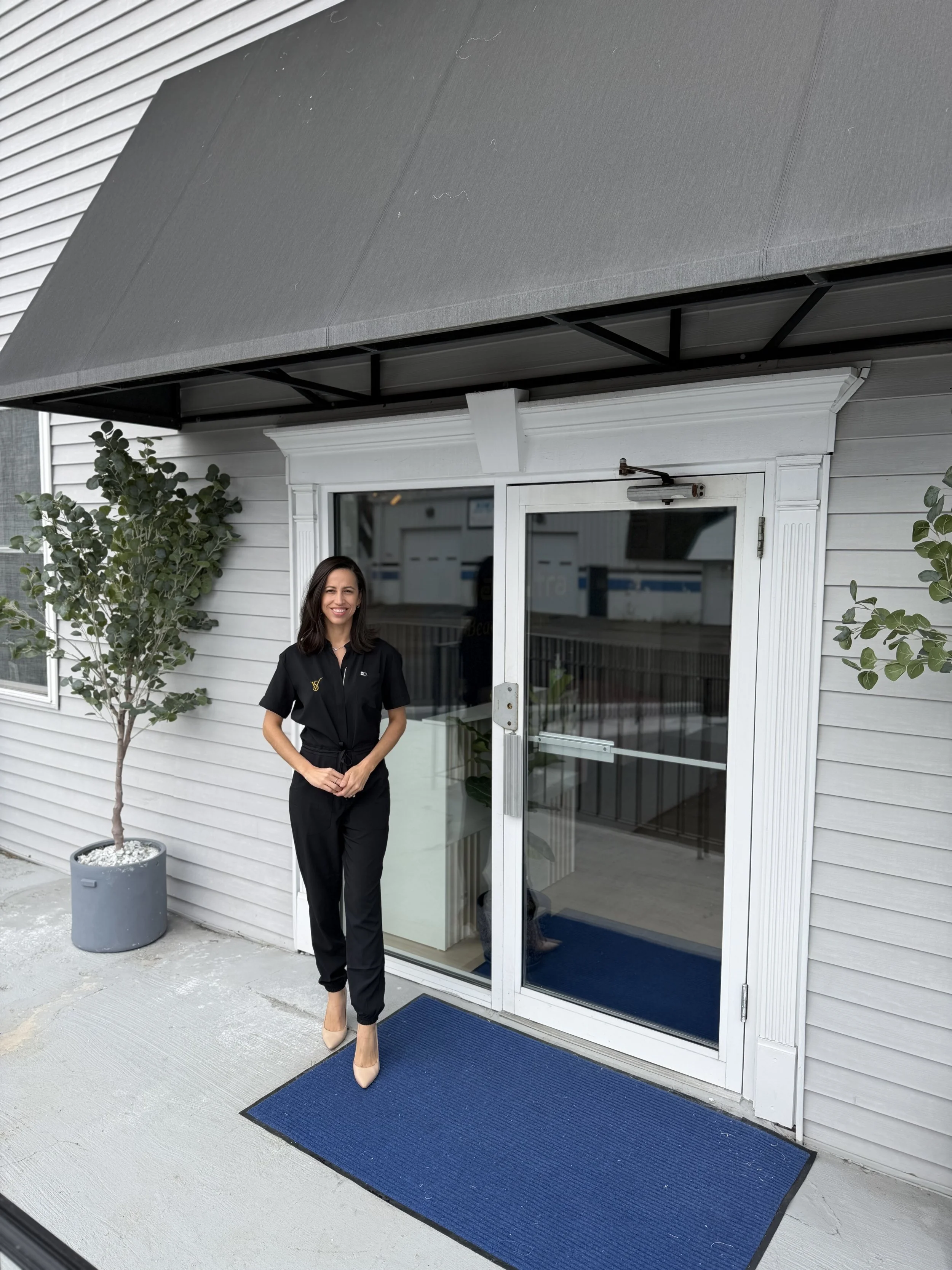 Cassia Zablonski, owner of Vitalis Luxe Spa in Medford MA, standing outside the spa storefront welcoming new skincare clients