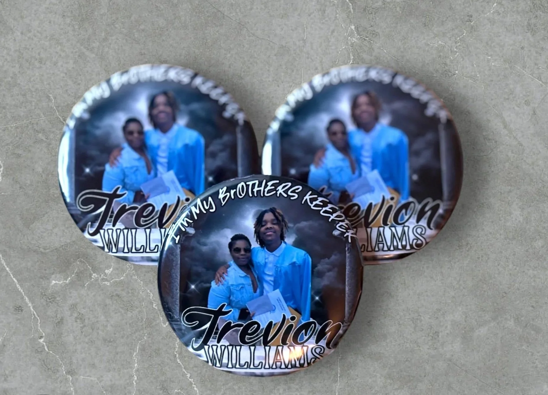 Three buttons featuring a portrait of a young man and woman, with the words "Trevin Williams" and "FAMILY MY BROTHERS KEEPERS" on a dark, cloudy background.