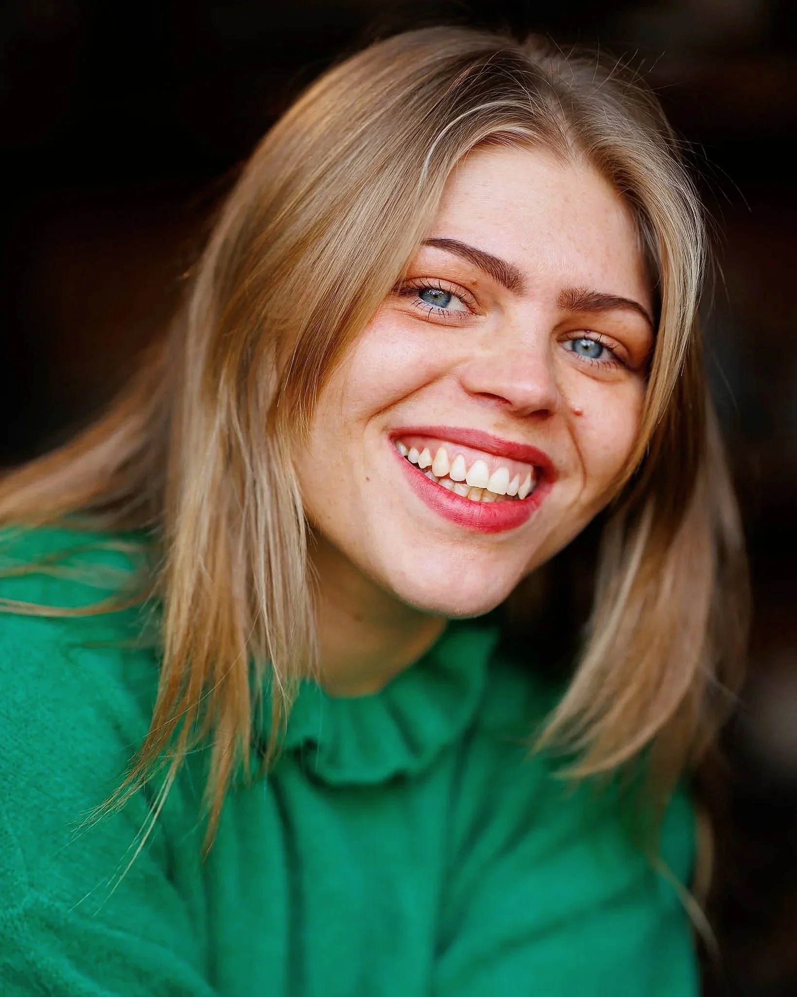 Close-up of a smiling woman with blonde hair, blue eyes, and fair skin wearing a green top.