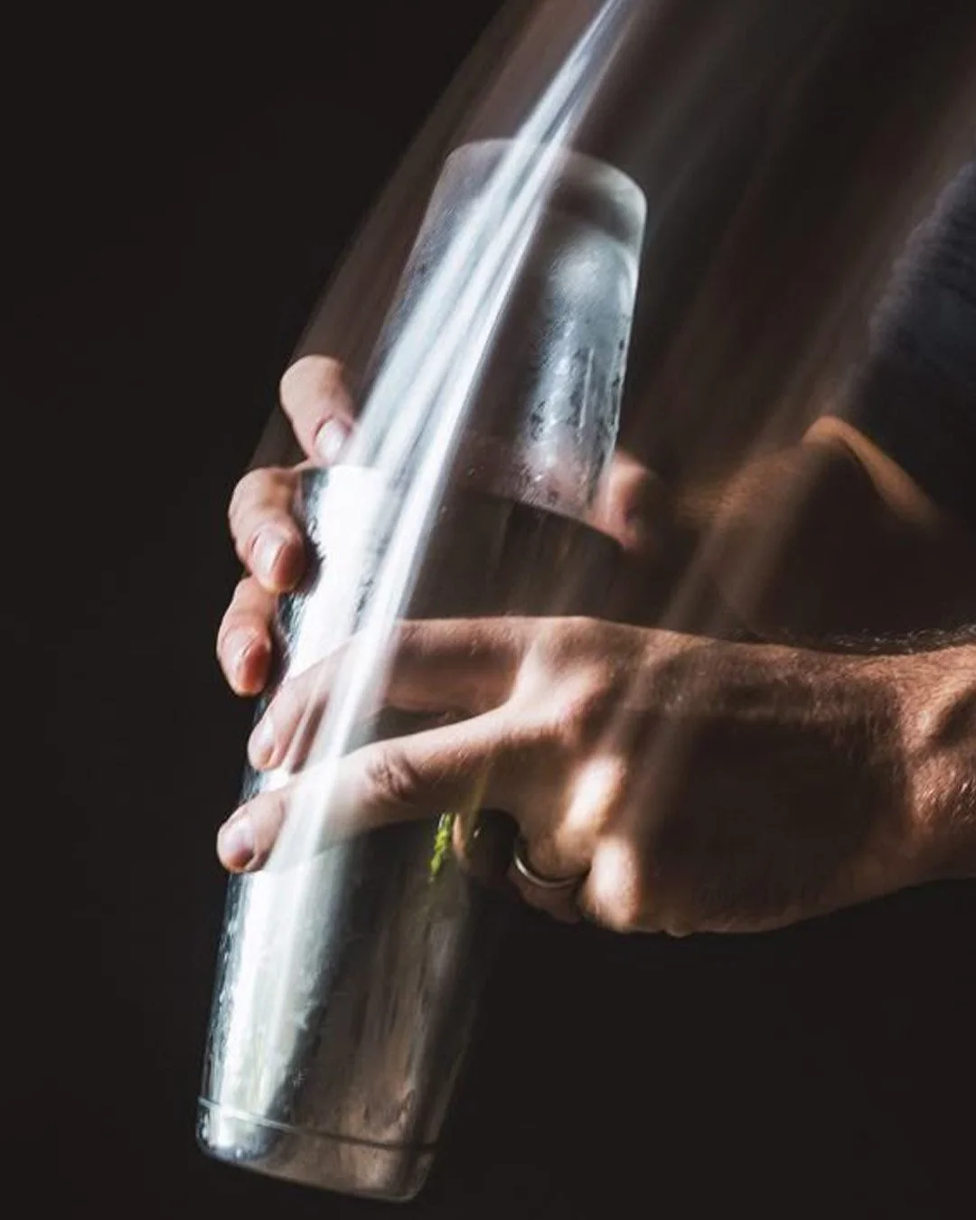 Close-up of a person holding a stainless steel cocktail shaker with condensation on its surface, against a black background.
