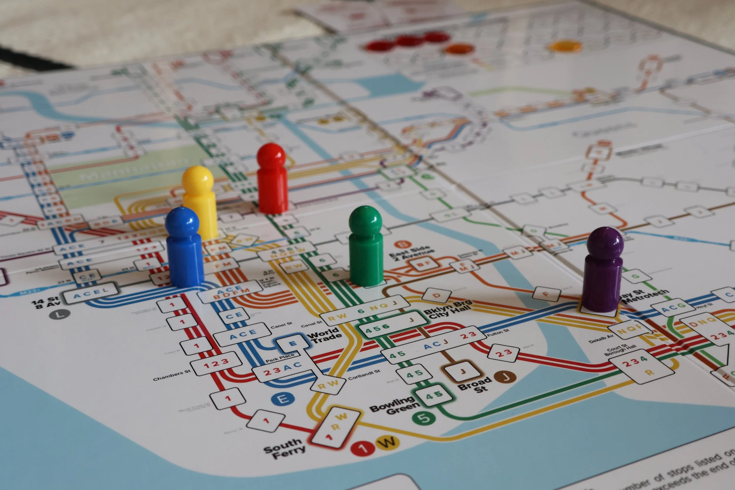 Colorful subway map with four game pieces (blue, yellow, red, green, purple) placed on it.