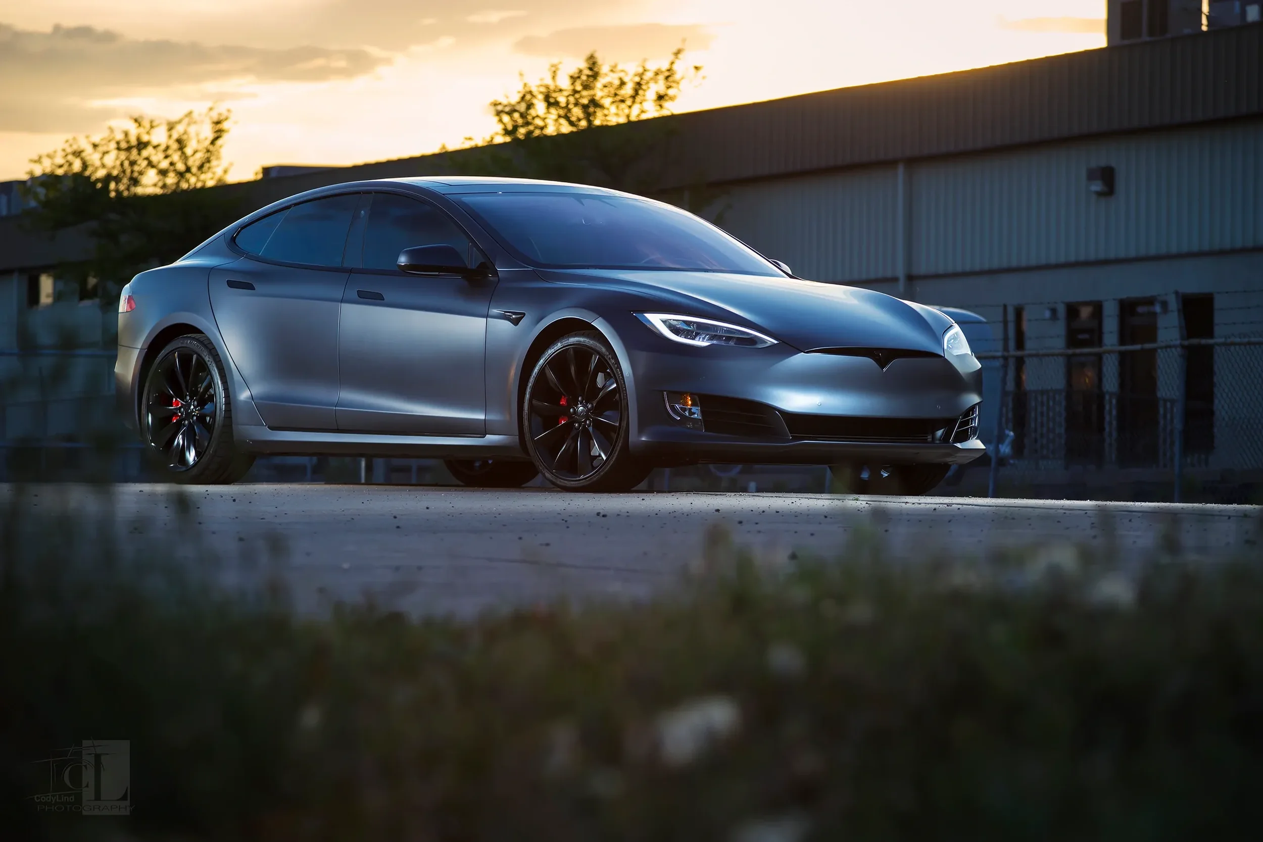 A sleek, silver Tesla Model S electric car parked outdoors during sunset with a low angle view.