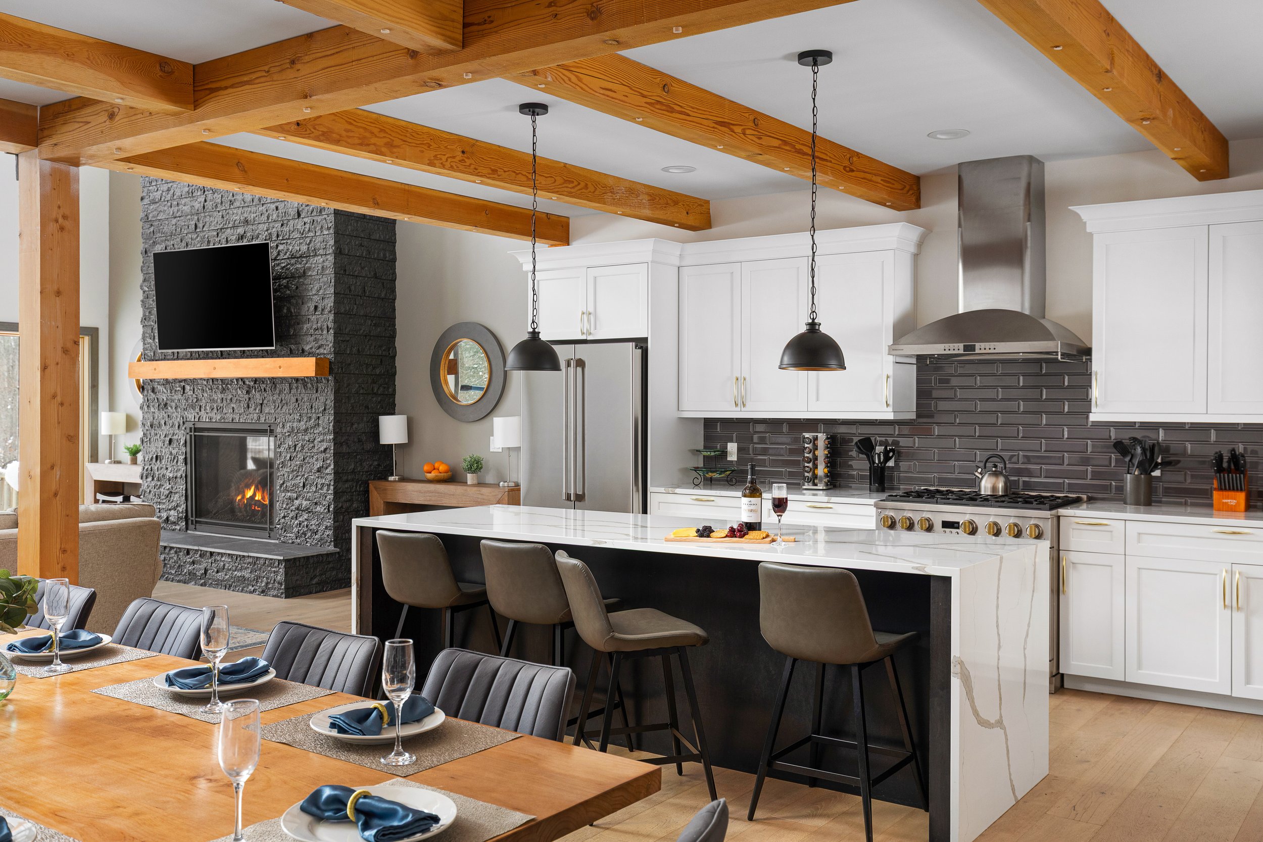 Modern kitchen with white cabinetry, gray backsplash, stainless steel appliances, black pendant lights, and a black stone fireplace with a mounted TV