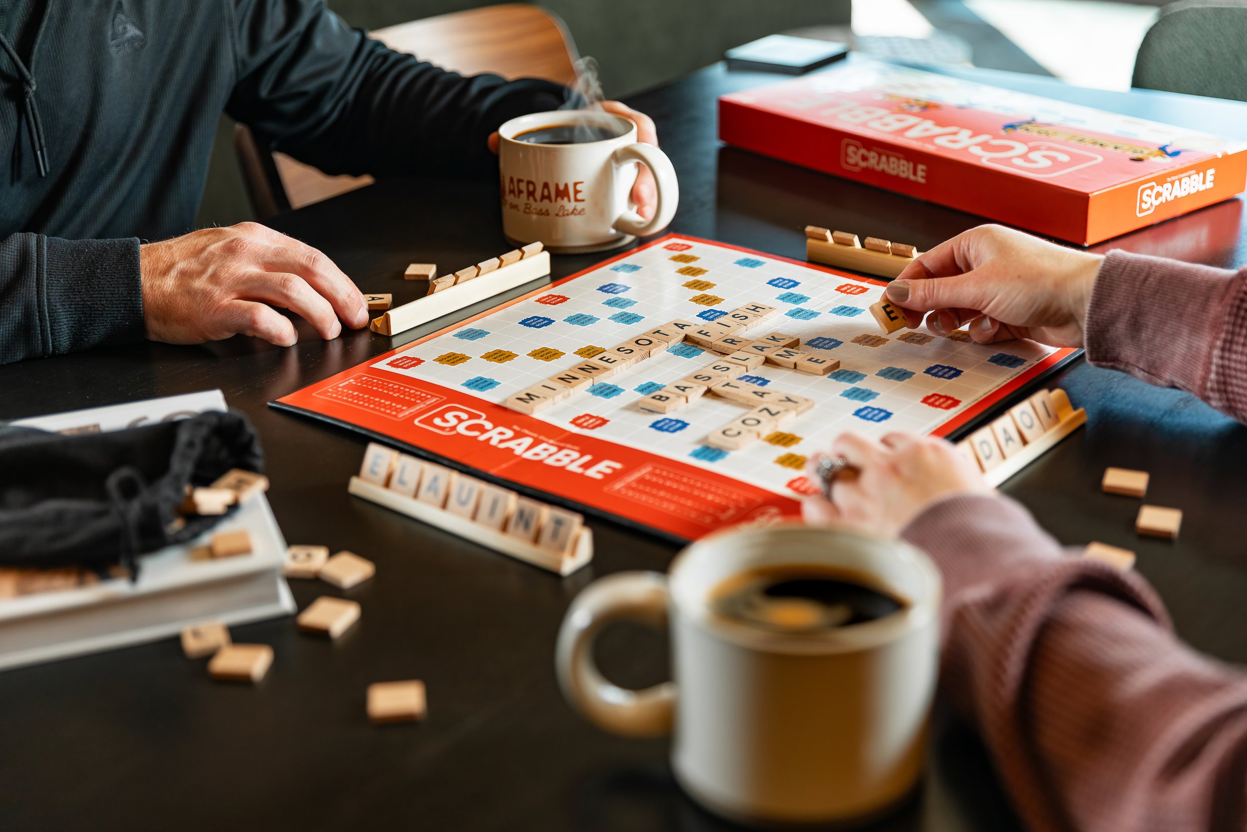 People playing Scrabble at a table with coffee mugs nearby.