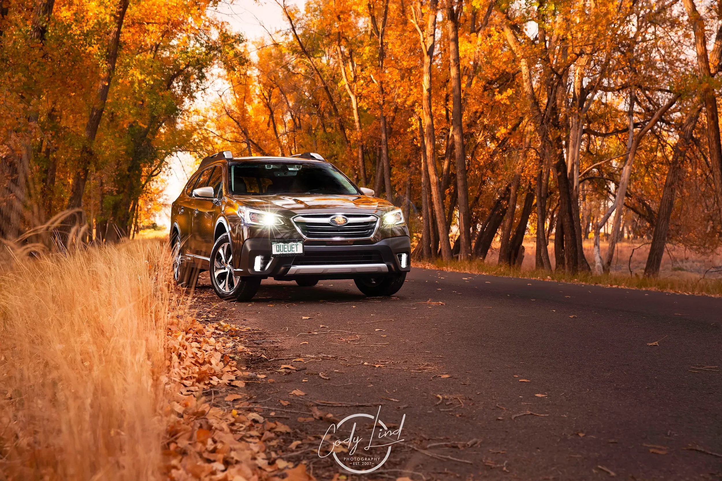 A black SUV parked on a rural road surrounded by autumn trees with orange and yellow leaves.