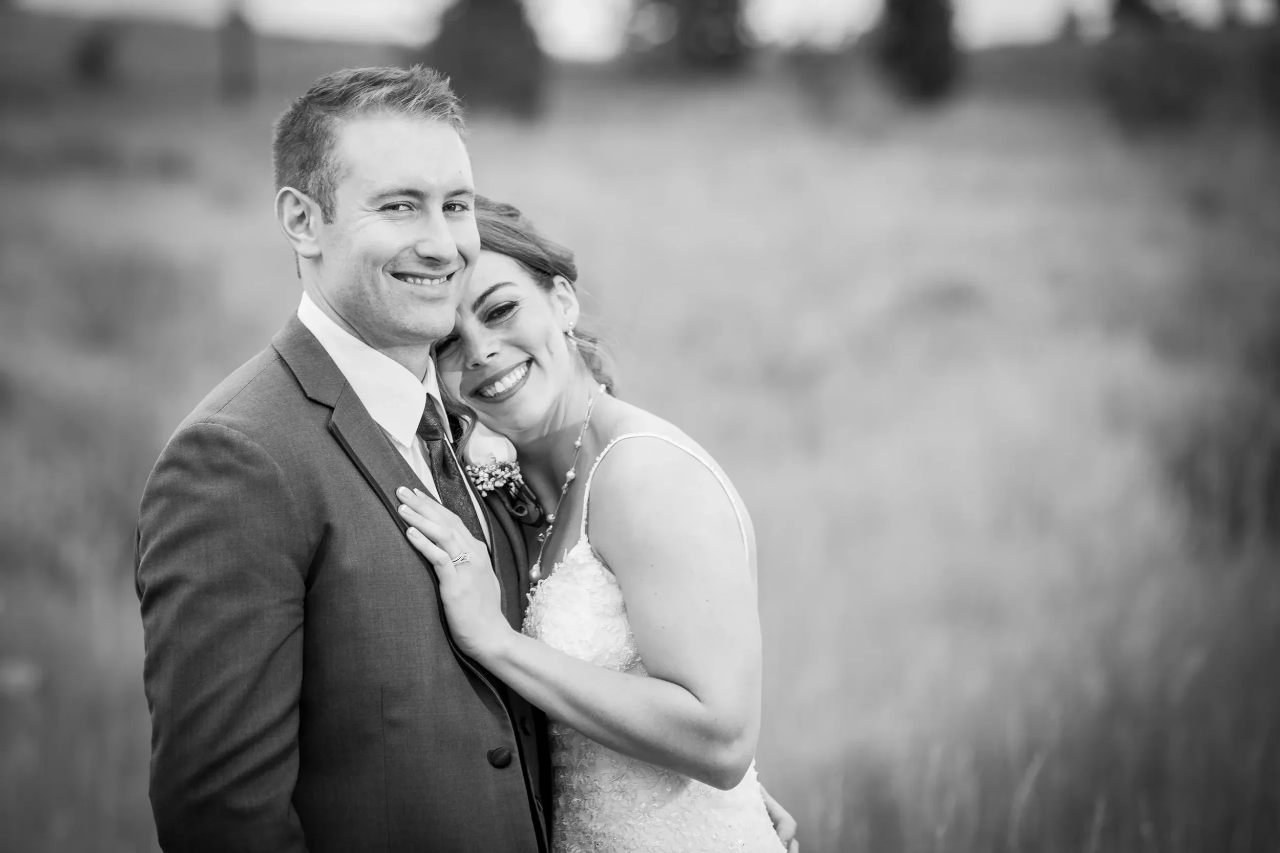 Black and white photo of a happy bride and groom embracing outdoors, with trees and grass in the background.