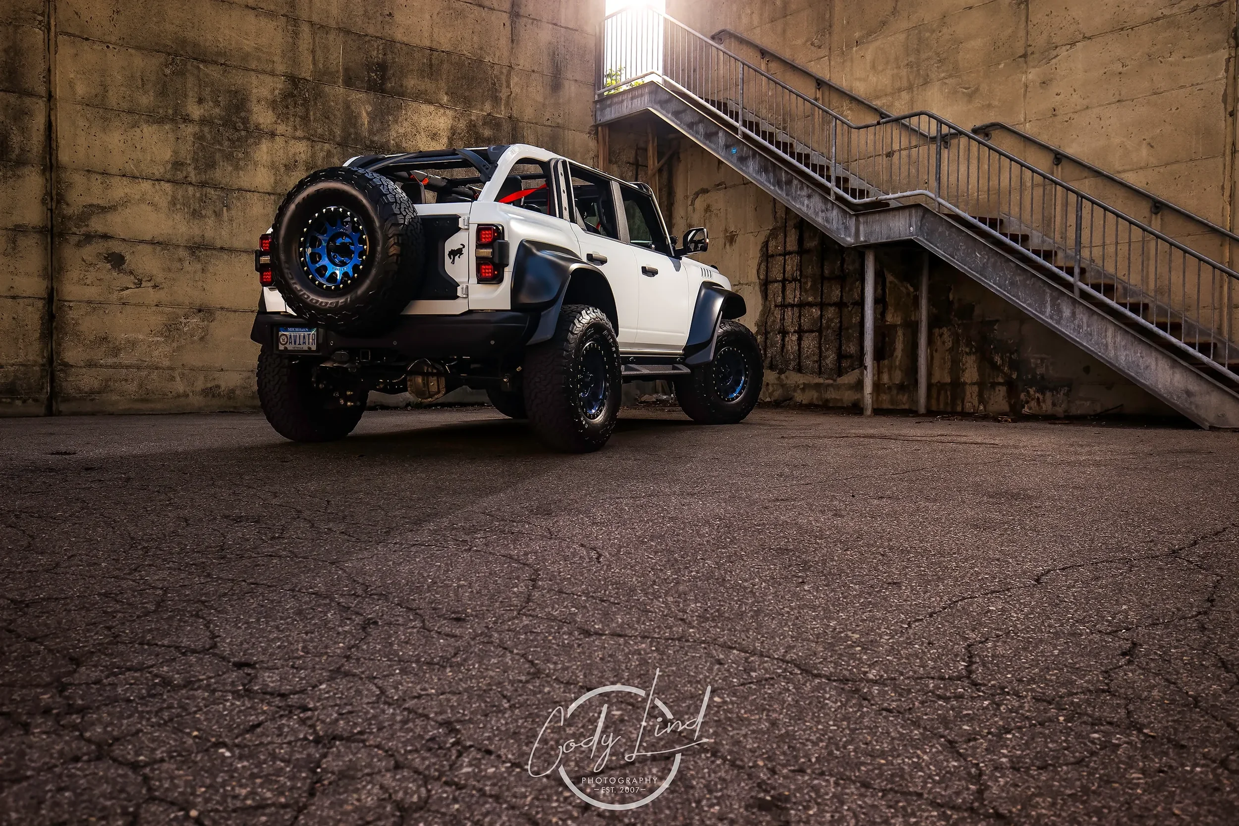 A white off-road vehicle with black accents parked in an underground parking lot, next to a concrete staircase leading upwards.