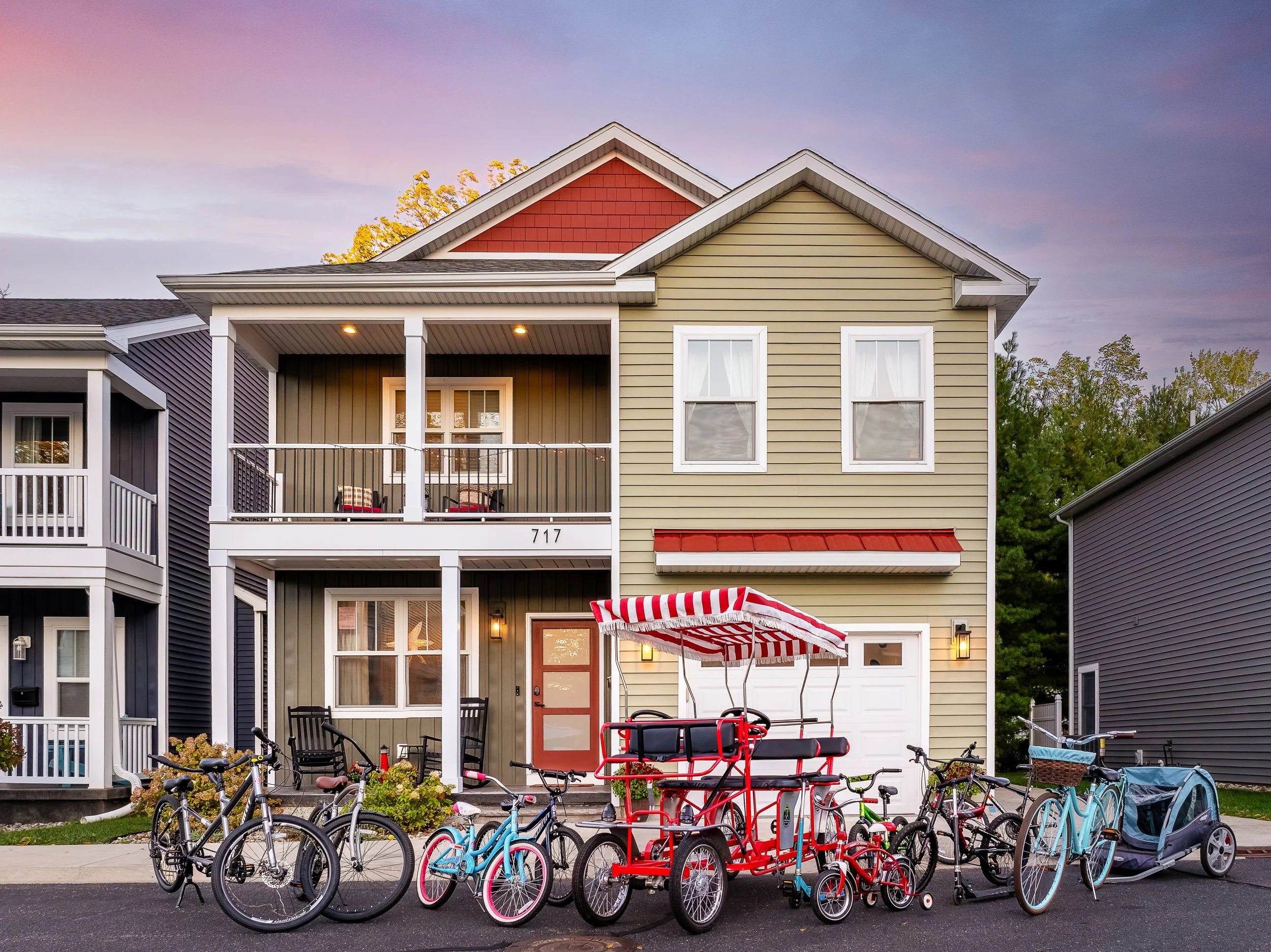 Multi-family residential building with a front porch, balconies, and multiple bicycles and a red pedal-powered tram in front.