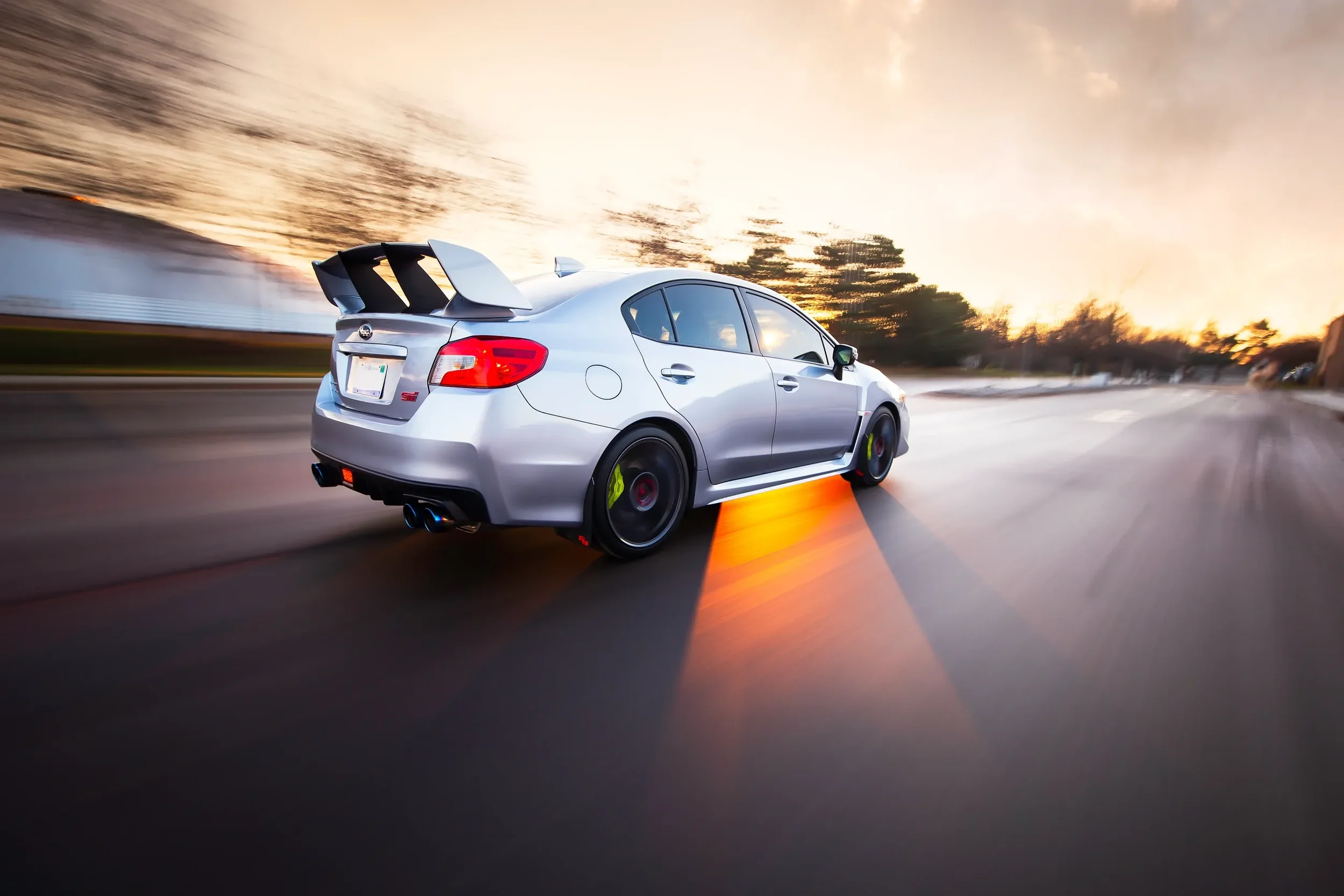 Silver sports sedan driving on a highway at sunset with motion blur and orange lighting effects.