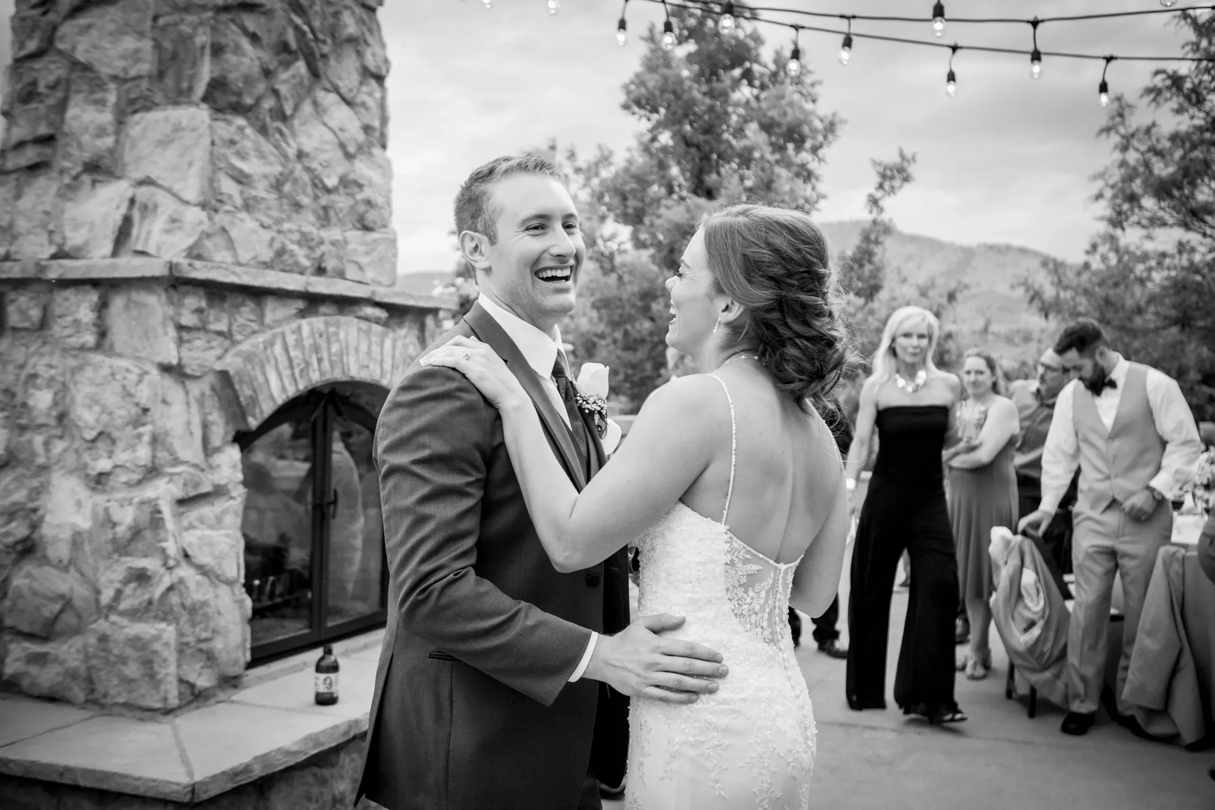 A couple in wedding attire dancing and smiling at their outdoor wedding reception, with guests in the background.