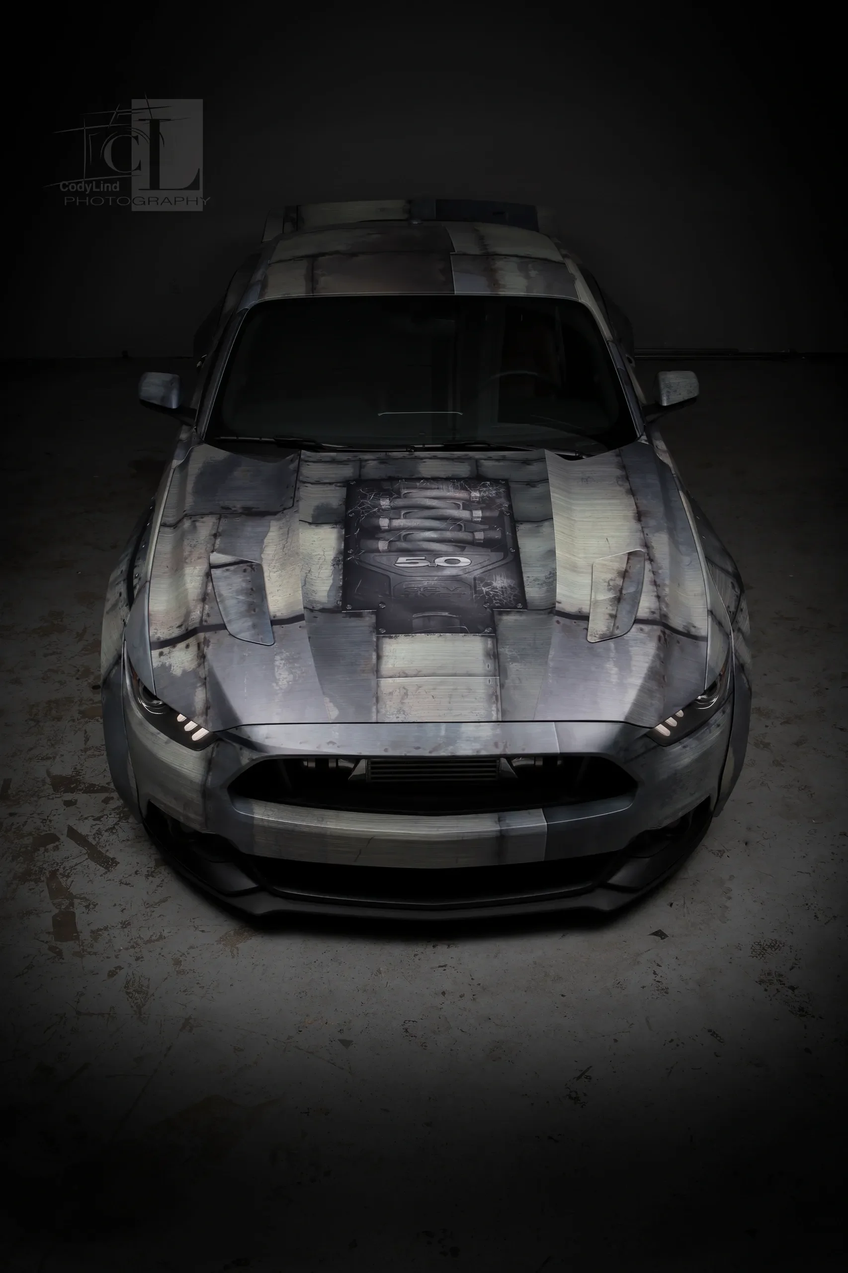 Top-down view of a sports car with a custom faux metal finish and a detailed hood graphic, parked in a dark garage.