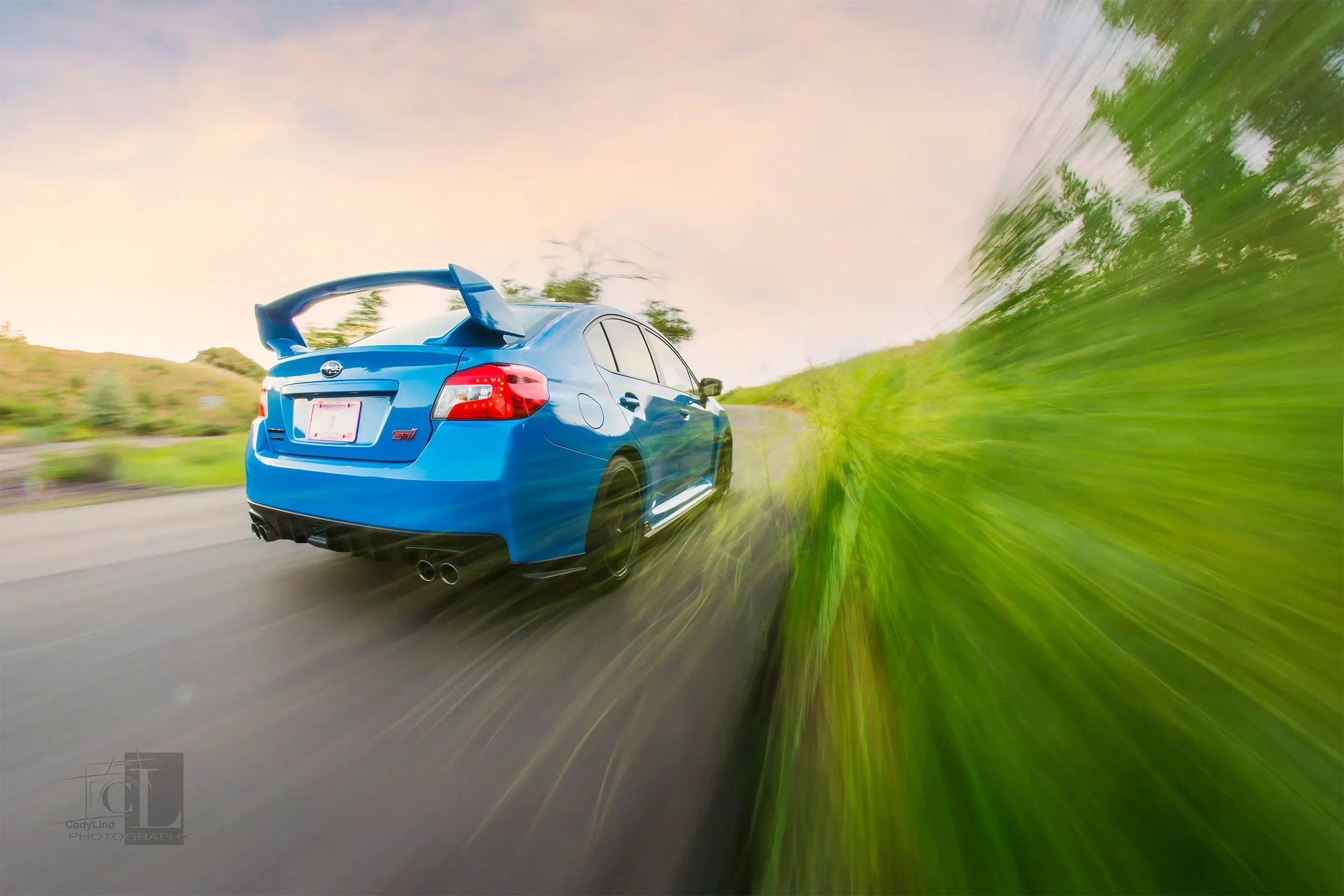 Blue Subaru Impreza WRX STI driving on a road with motion blur effect, greenery on the side, during sunset or sunrise.