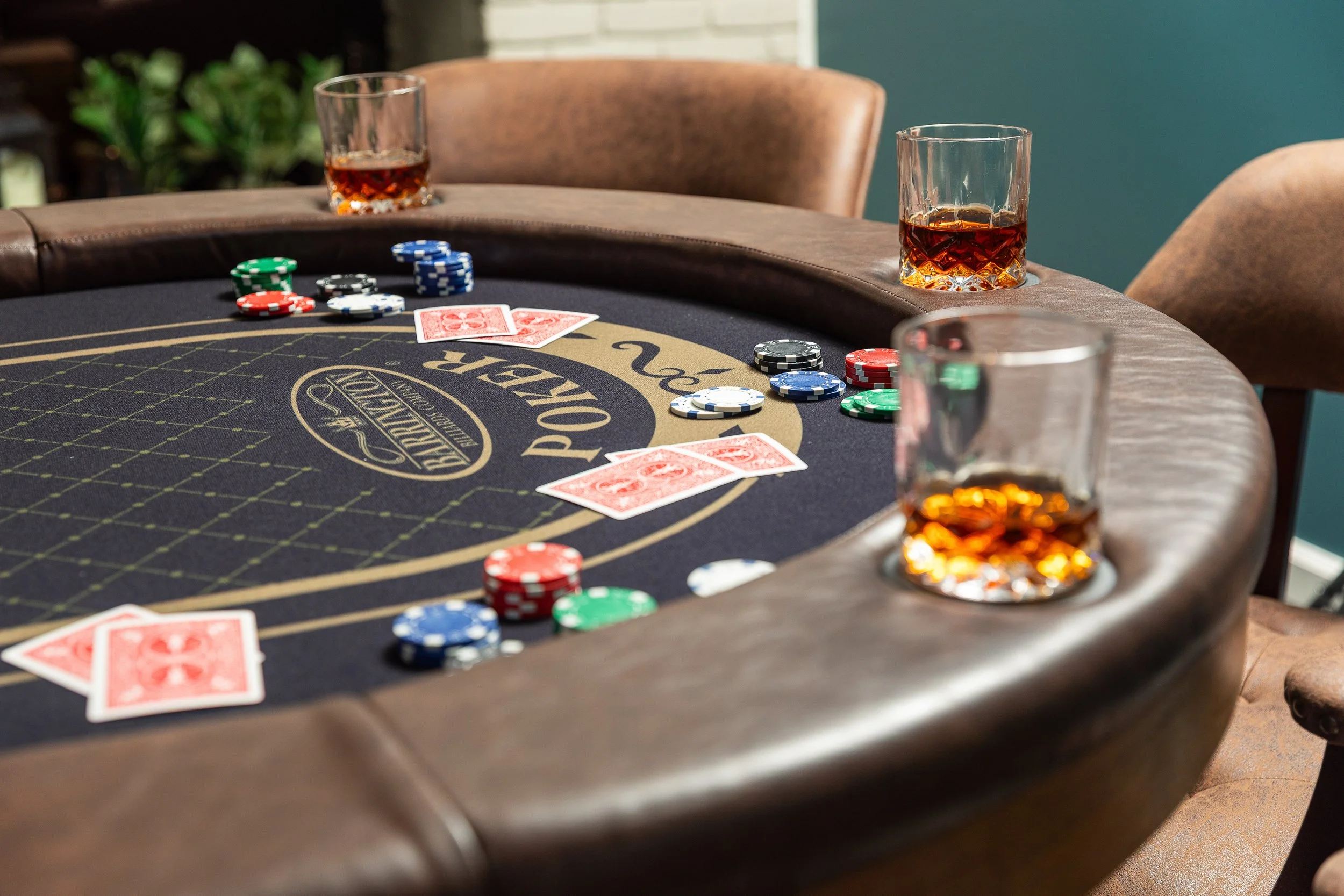 A poker table with poker chips, playing cards, and glasses of whiskey.