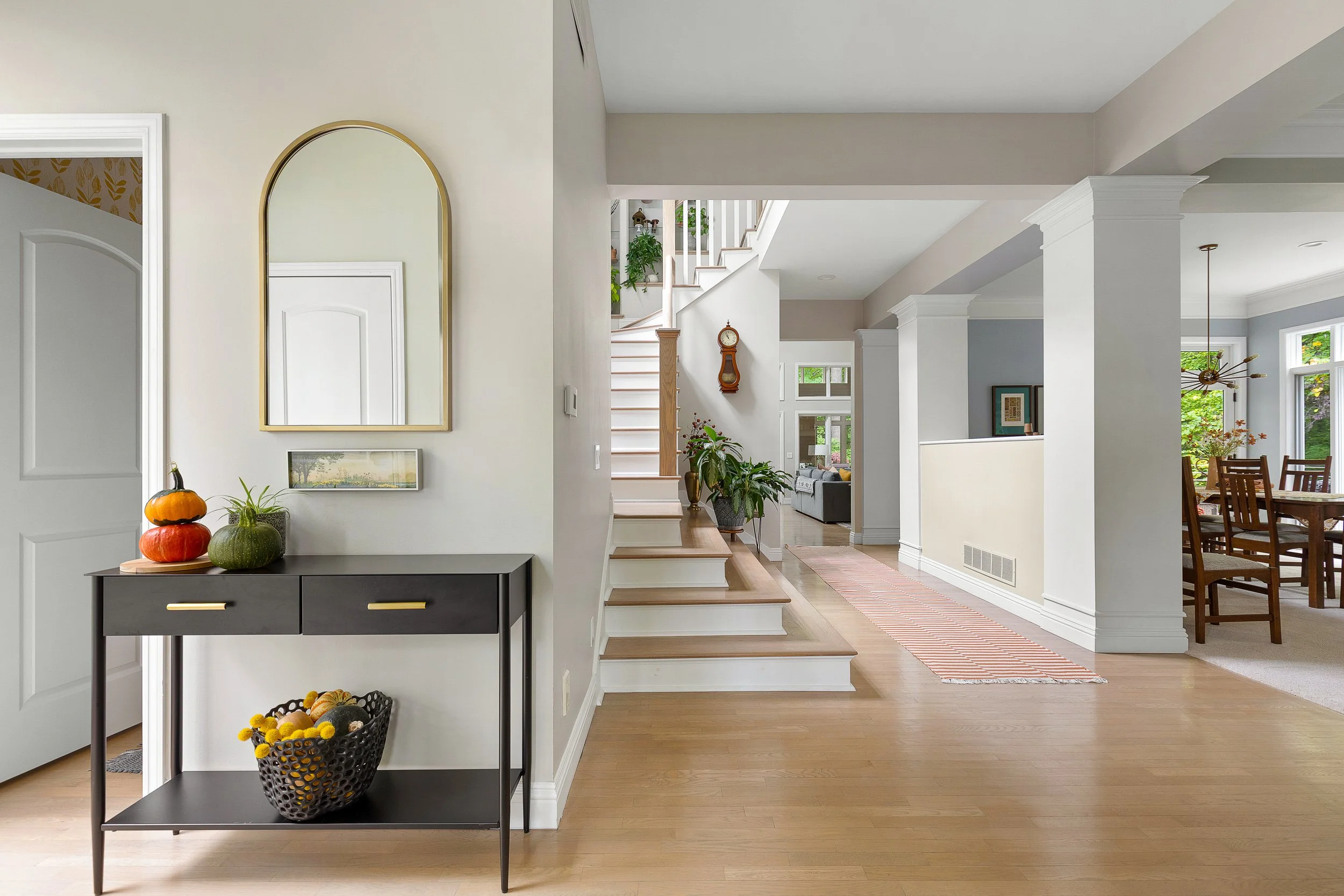 Interior view of a modern home with a hallway, staircase, and dining area, featuring light-colored walls, hardwood floors, and decorative plants.