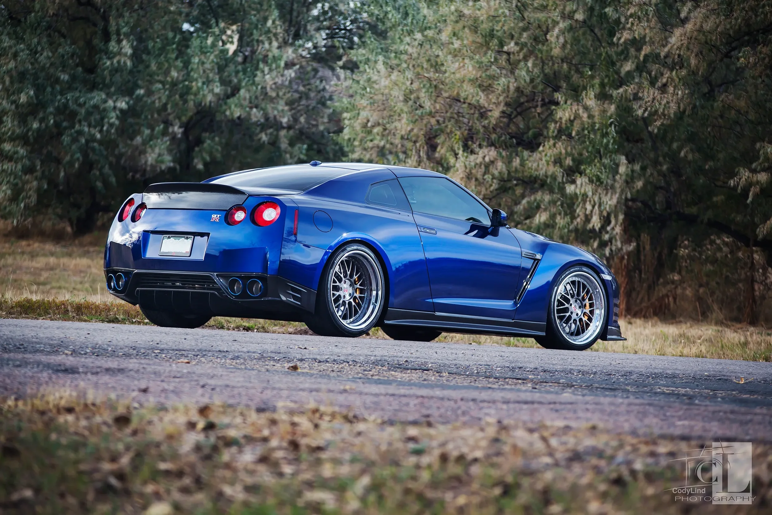 A blue sports car parked on a rural road with trees in the background.