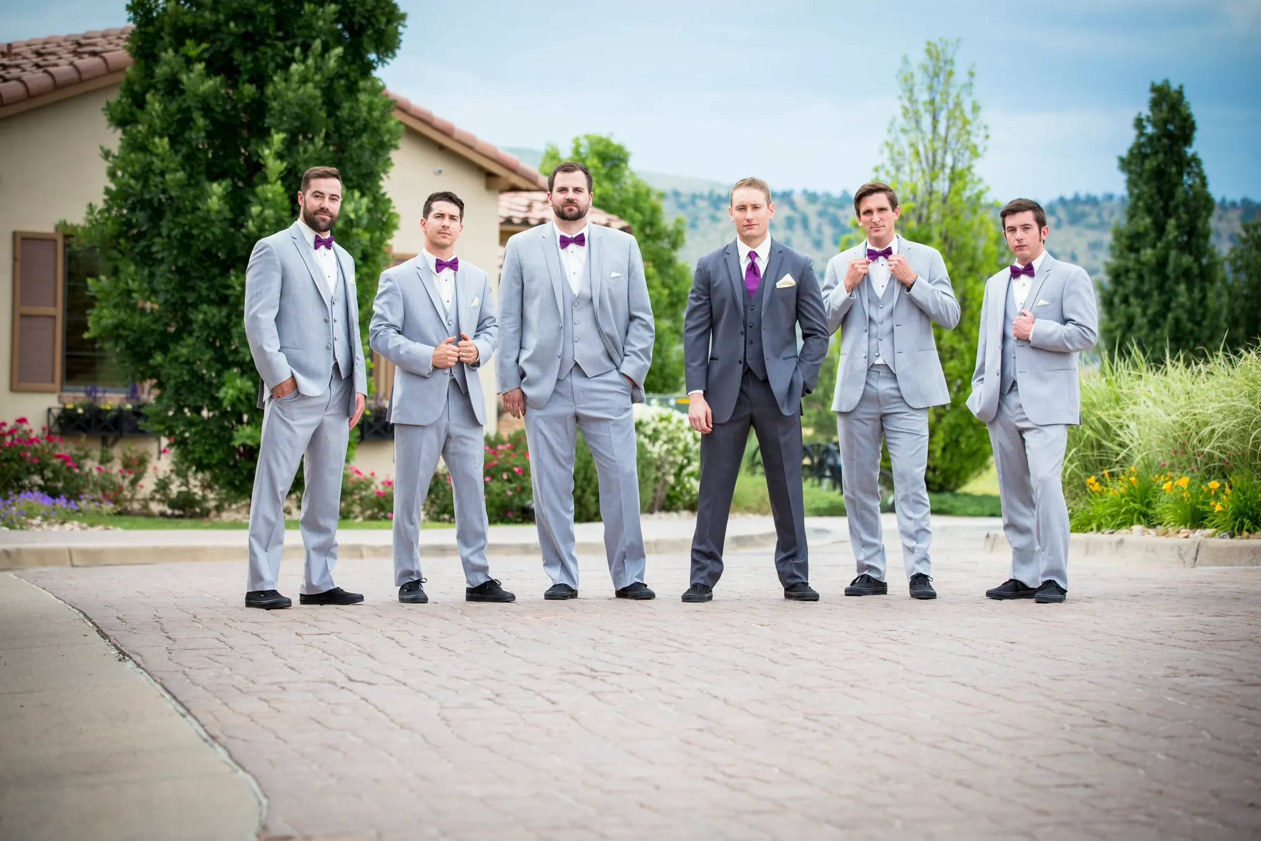 A group of seven men dressed in suits, standing outdoors in a landscaped area with a building and trees in the background.