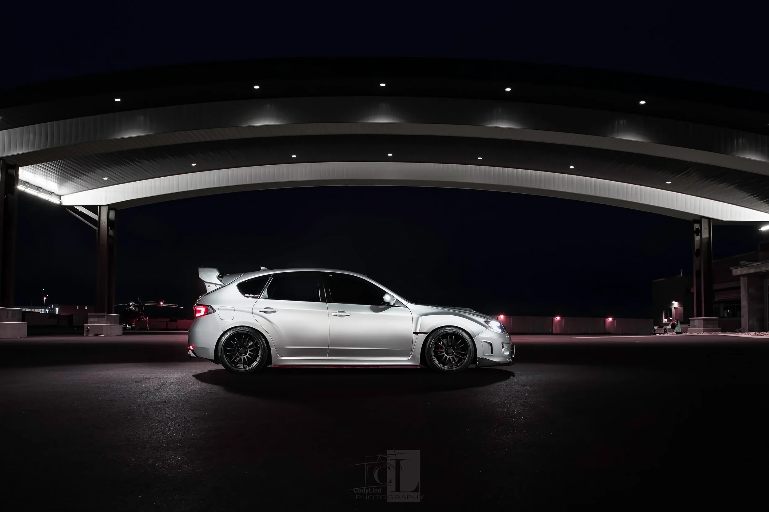 Silver sports car parked under a lit structure at night with a dark sky.