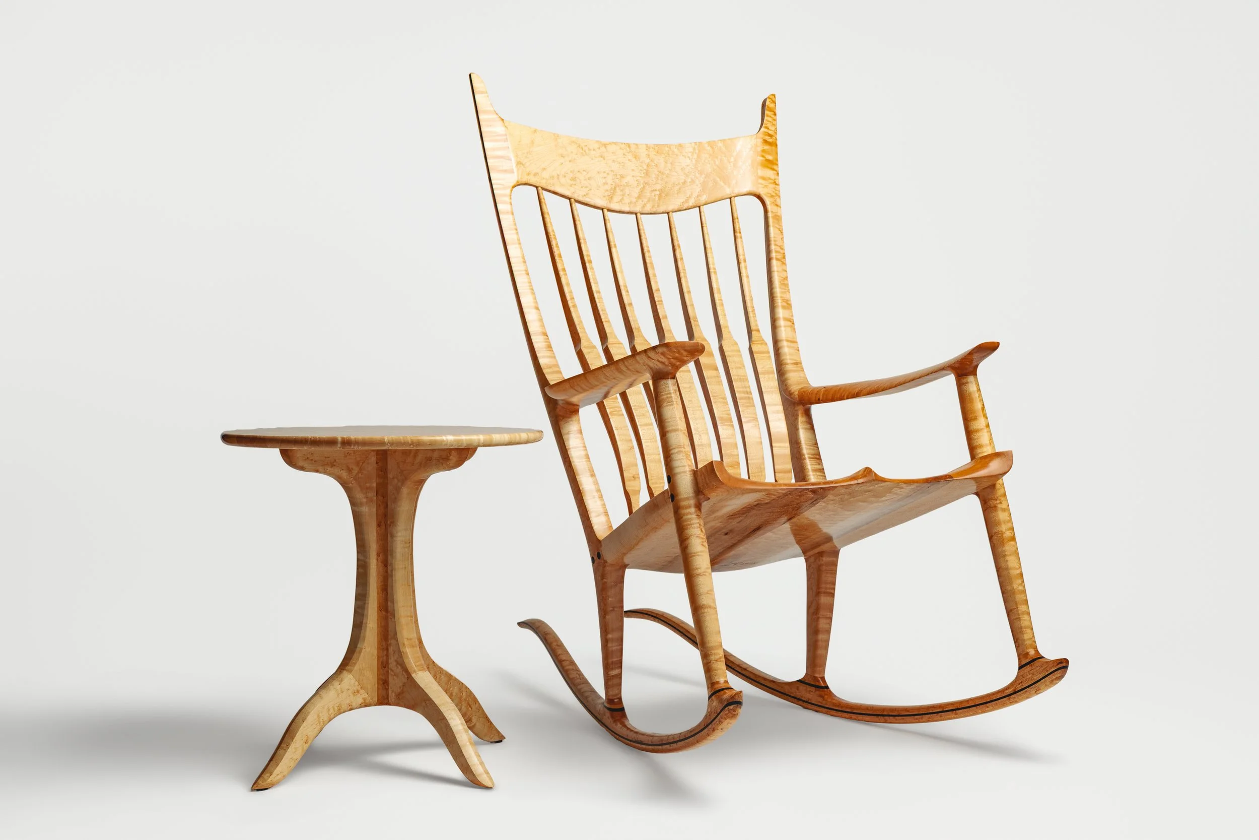 A wooden rocking chair with a high backrest and armrests, paired with a small round side table, set against a plain white background.