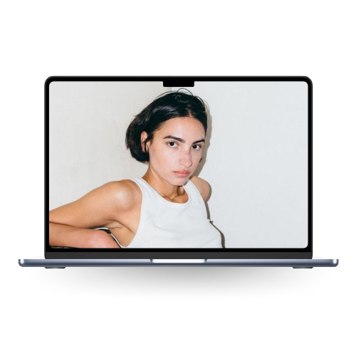 A woman with dark hair and a white tank top appears on a laptop screen, looking directly at the camera.