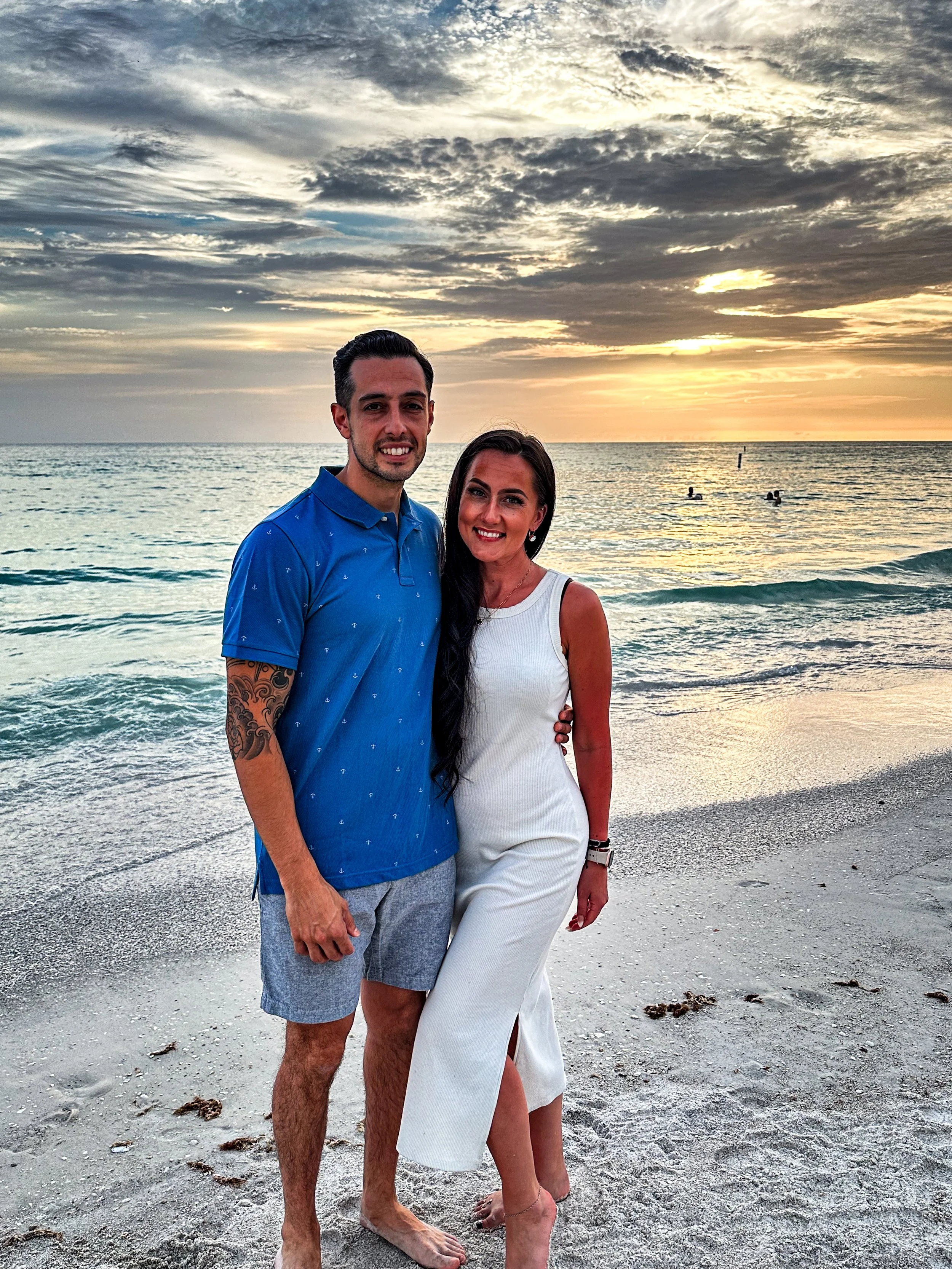 A couple standing on the beach during sunset with the ocean in the background.