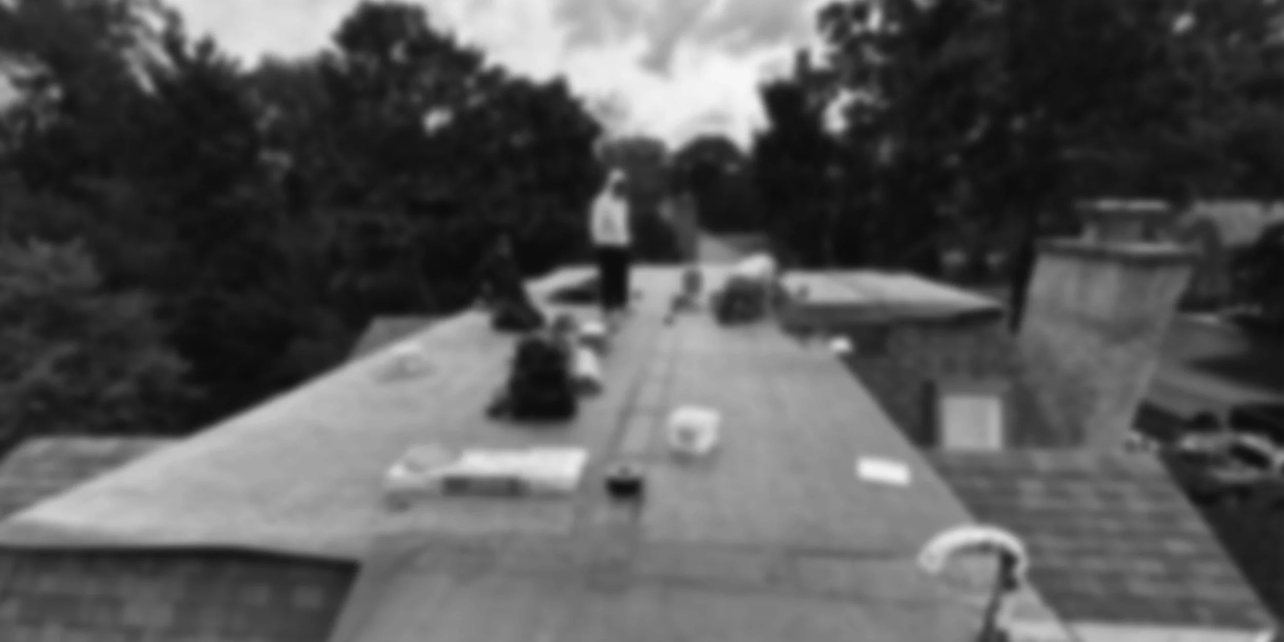 A long outdoor table set up on a rooftop with people and various items placed on it, surrounded by trees and buildings in the background.
