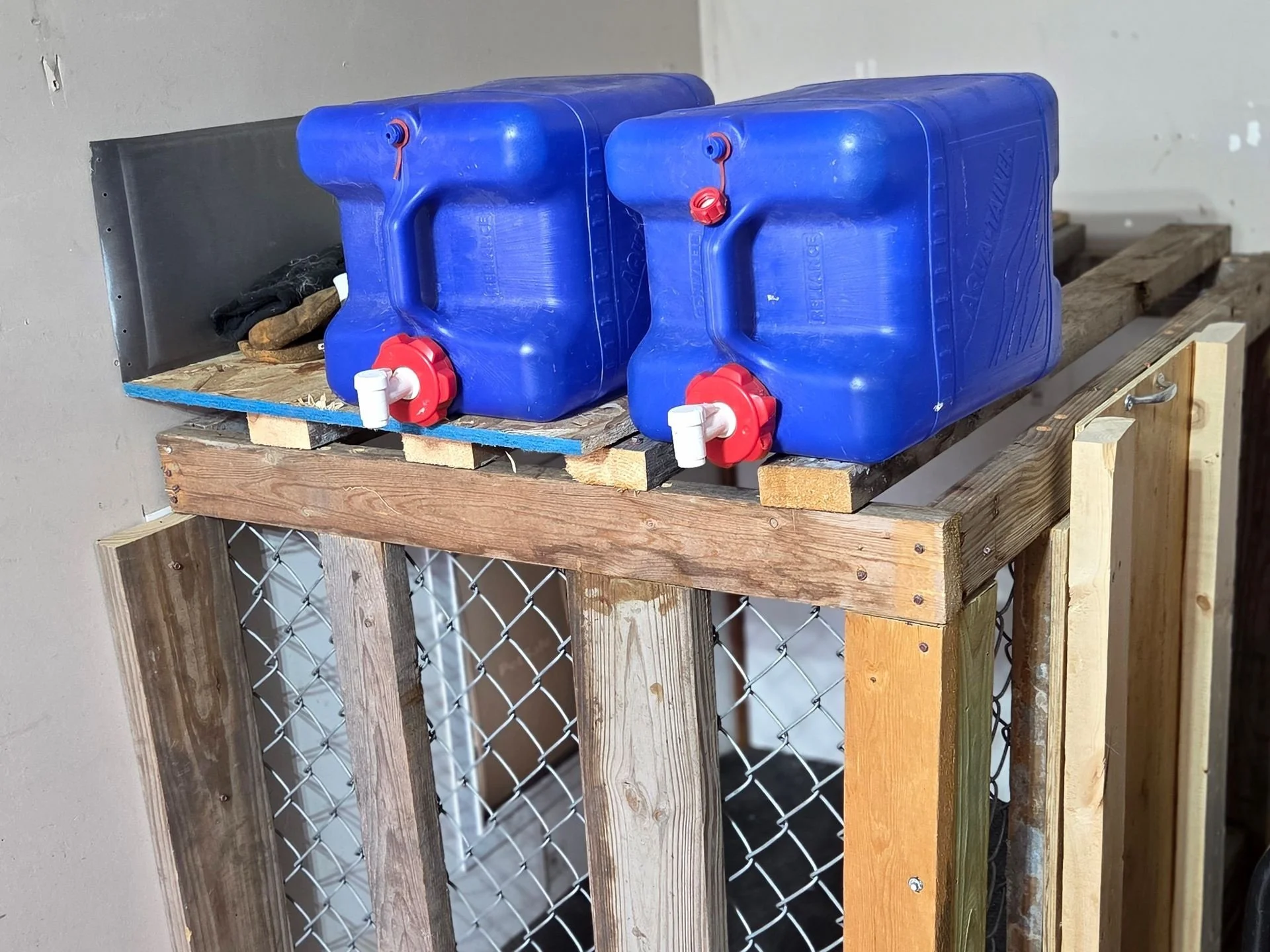 Two blue plastic water containers with red caps and white spouts are placed on a wooden platform in a partially constructed or repaired area.