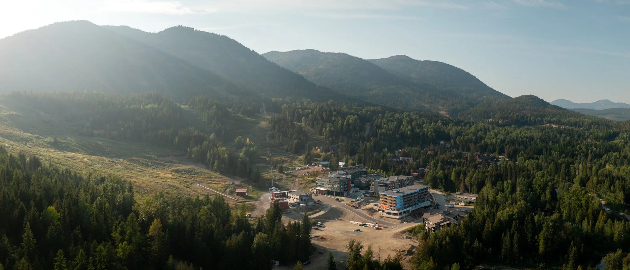 RED Mountain Resort in Rossland, BC - A mountain town surrounded by lush green forests with mountains in the background under a clear sky.