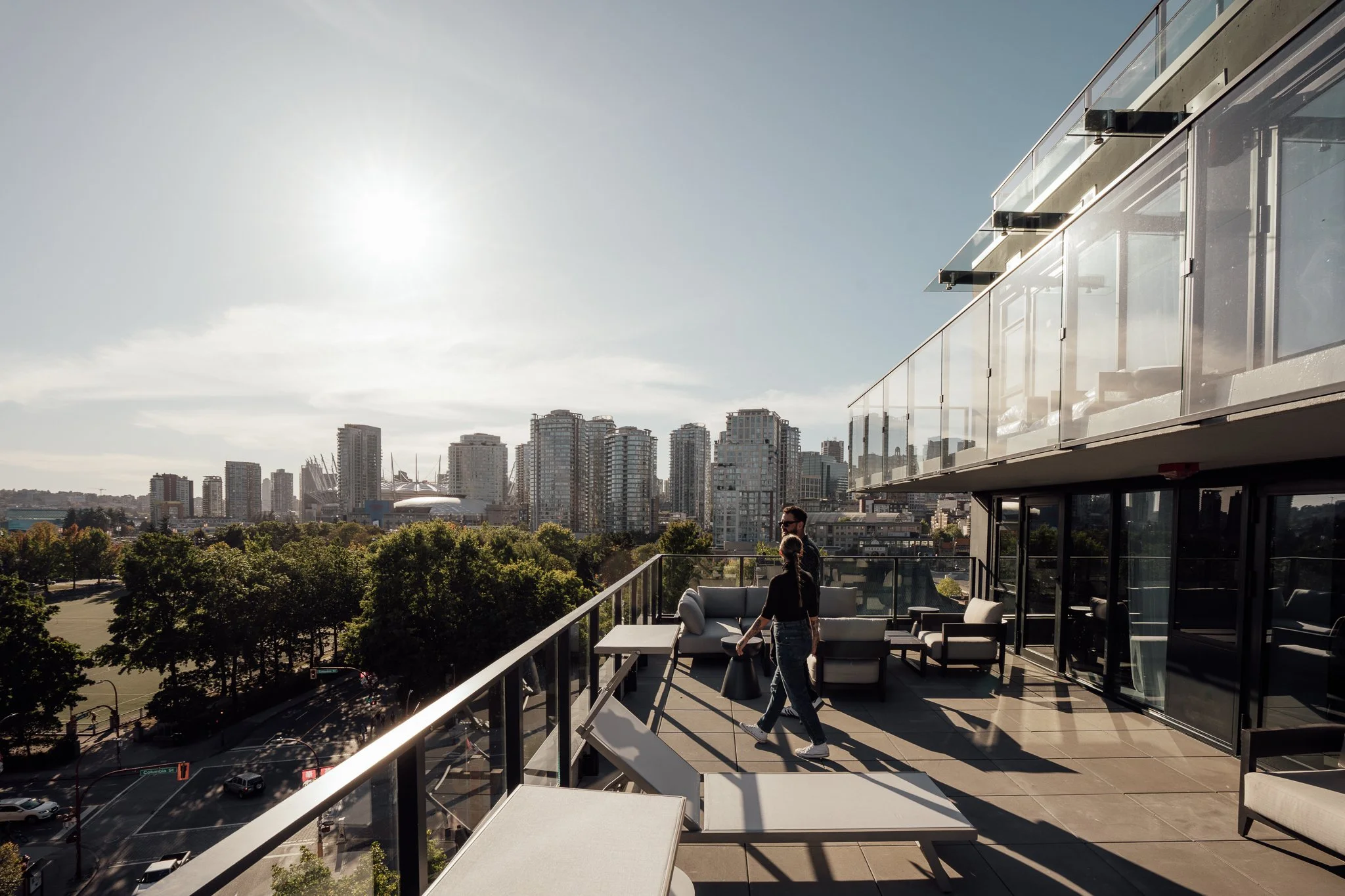 People on a balcony at Keefer House overlooking the Vancouver city skyline with modern high-rise buildings and trees, during daytime.
