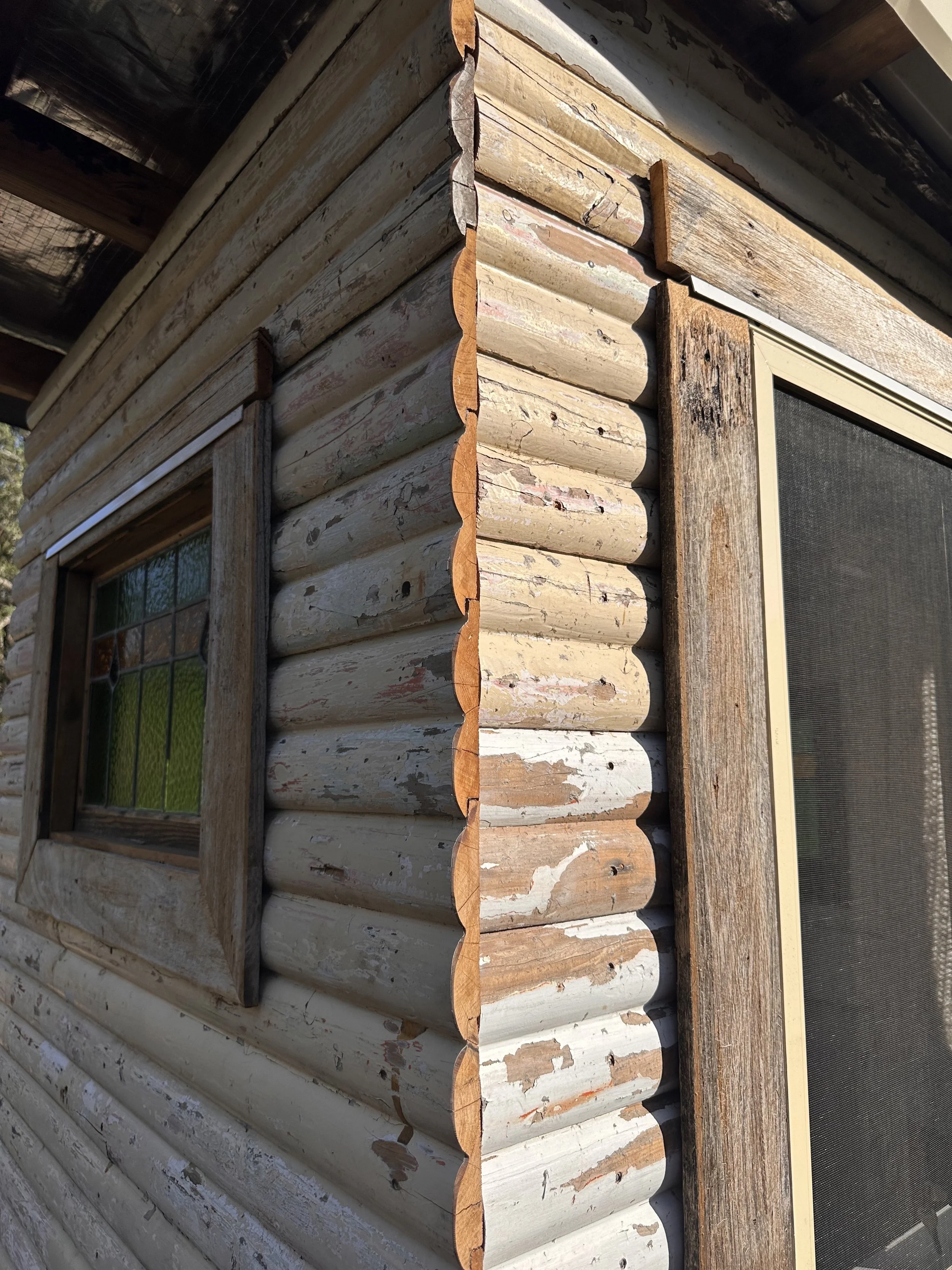Close-up of a corner of a rustic log cabin with aged wood siding and trim, and small window.