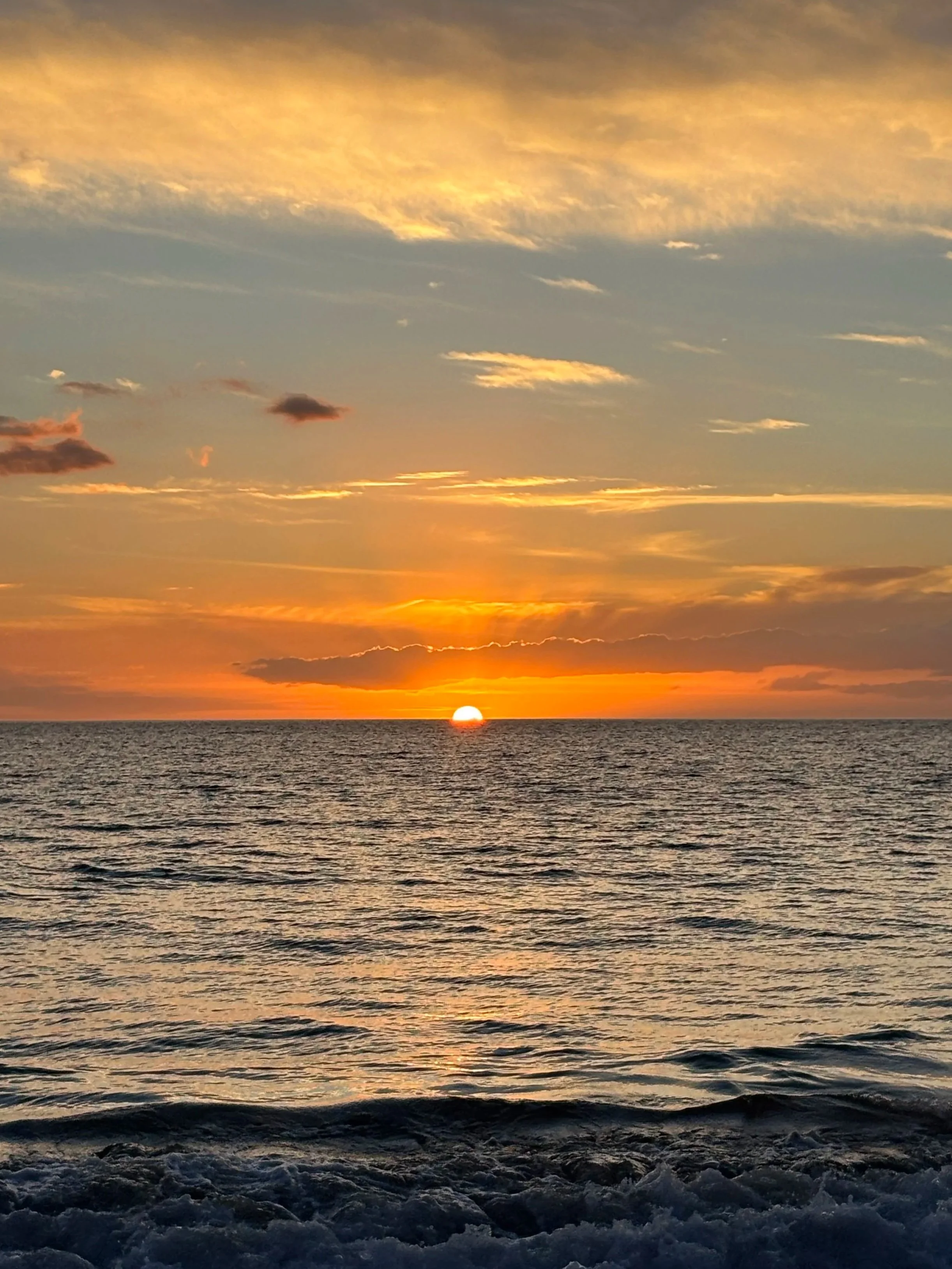 Sunset over the ocean with clouds in the sky and gentle waves on the water.