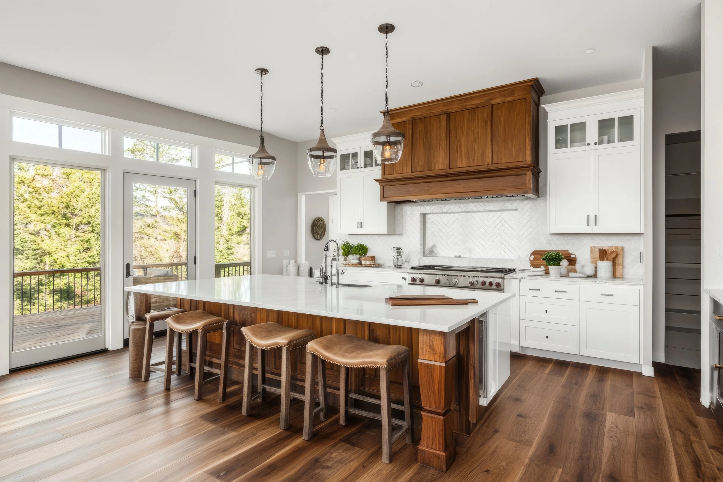 Modern kitchen with island, hanging pendant lights, white cabinets, and a sliding glass door leading to a deck.