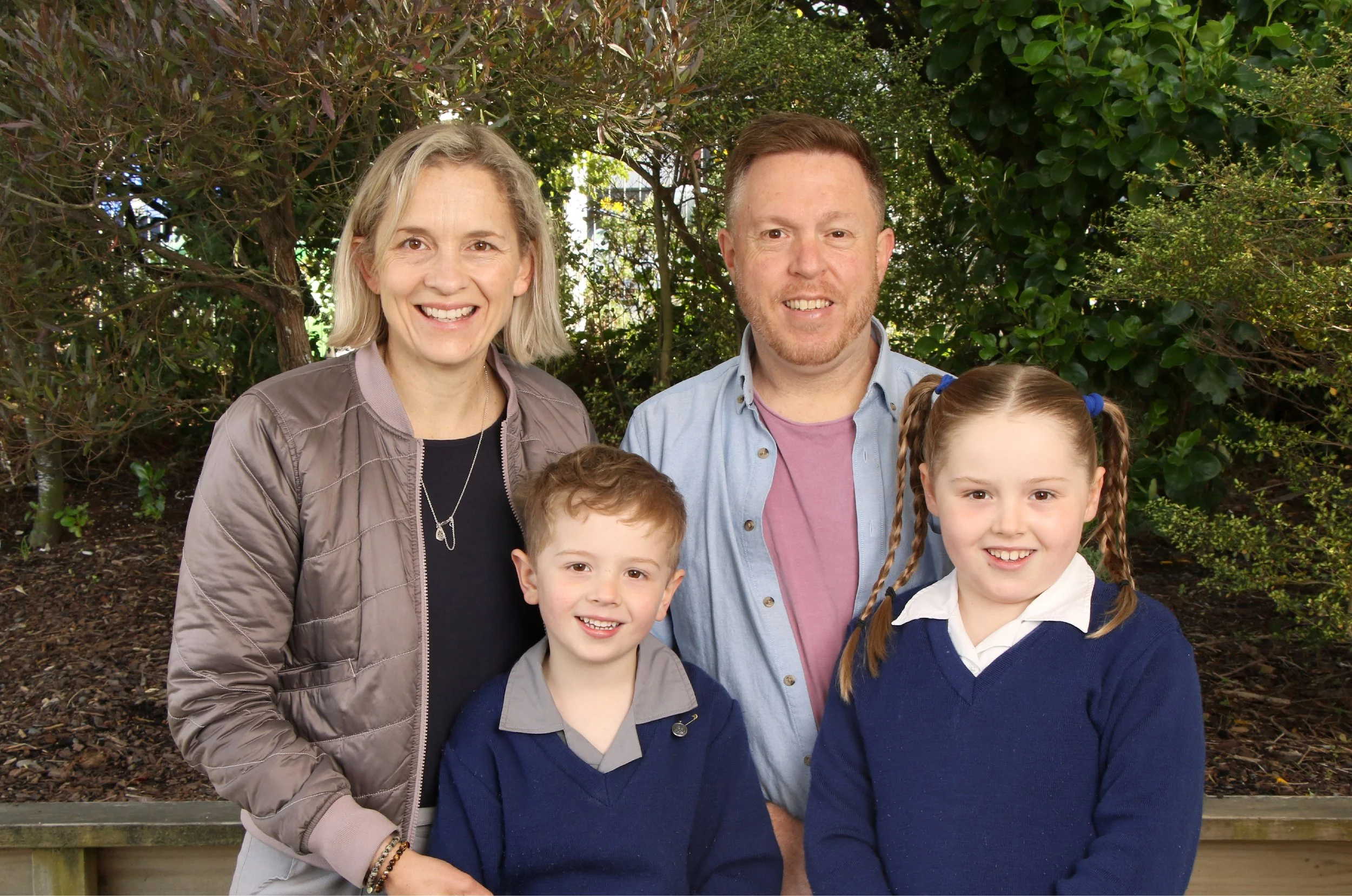 Smiling family of five standing outdoors in front of bushes and trees