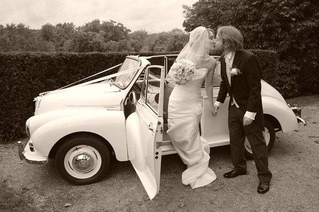 Bride and groom kissing in front of a vintage car.