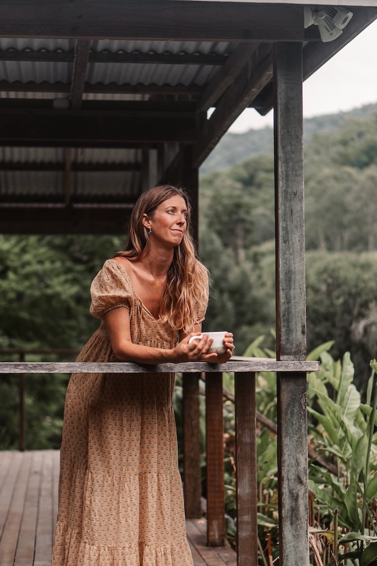 Woman resting with tea overlooking nature, representing calm, balance and holistic wellbeing in the Gold Coast hinterland
