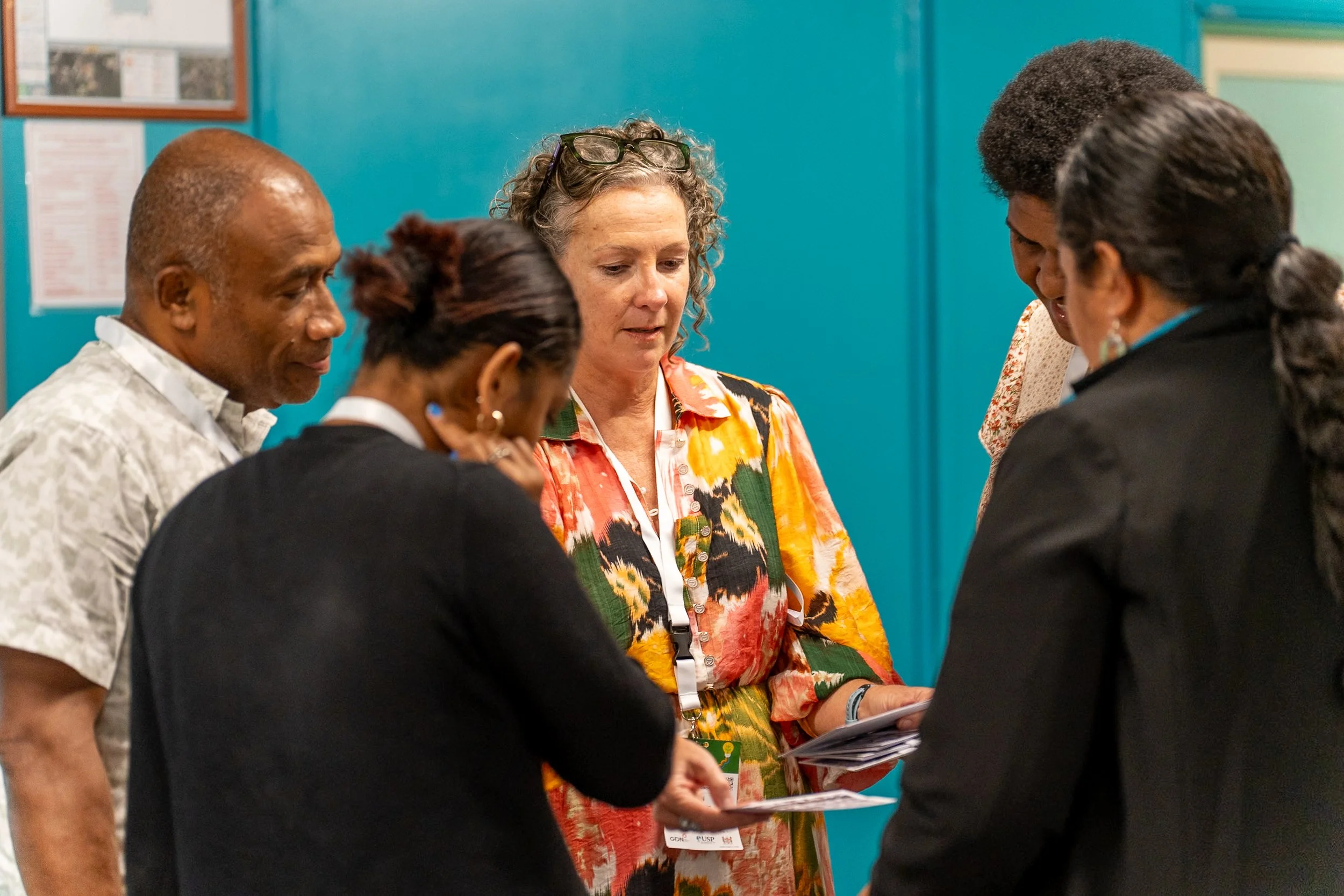 Group of five people standing close together, looking at papers or documents, in a room with a blue wall.
