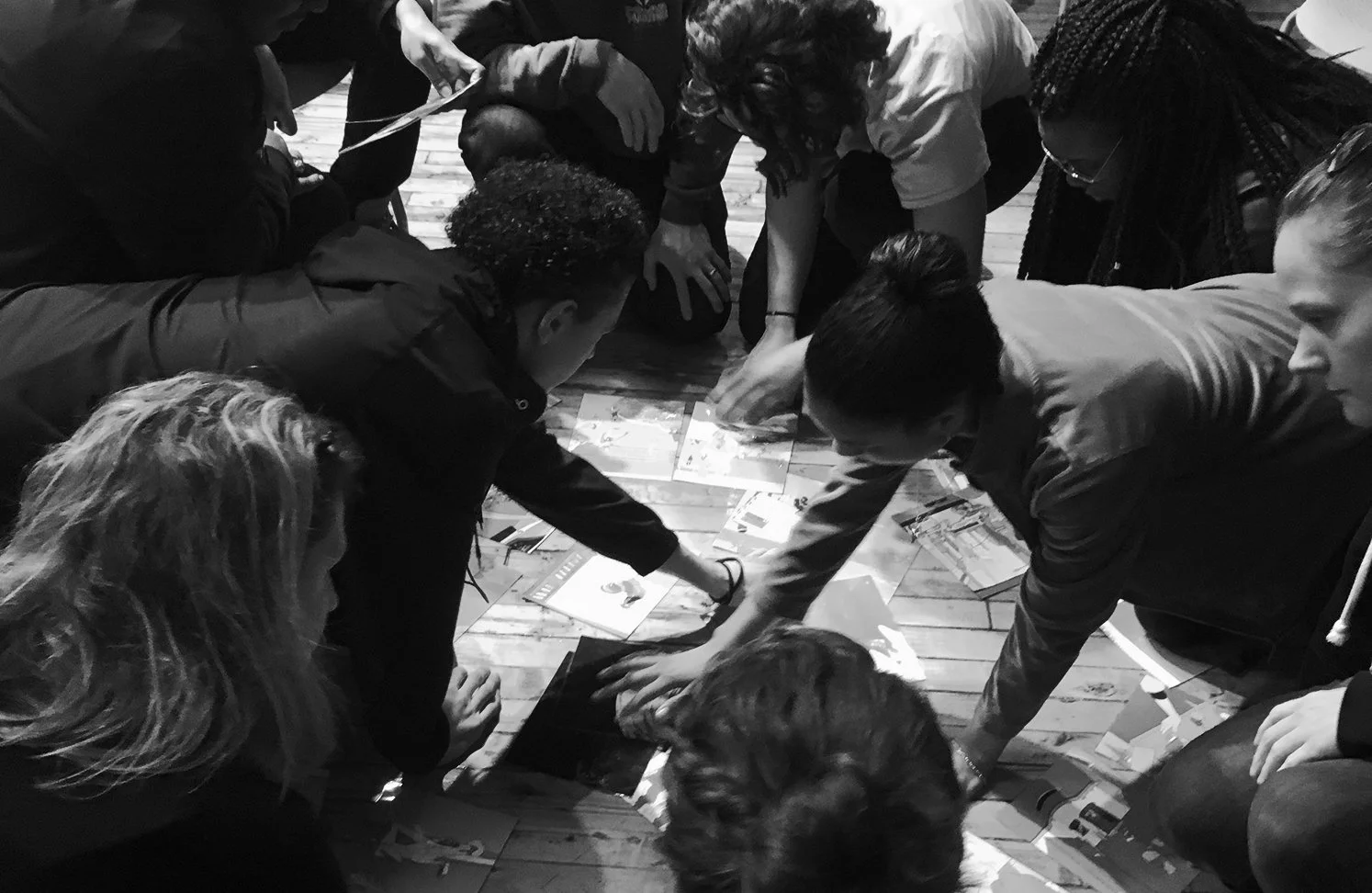 Group of people gathered around and reaching towards a collection of pictures and papers on the floor.