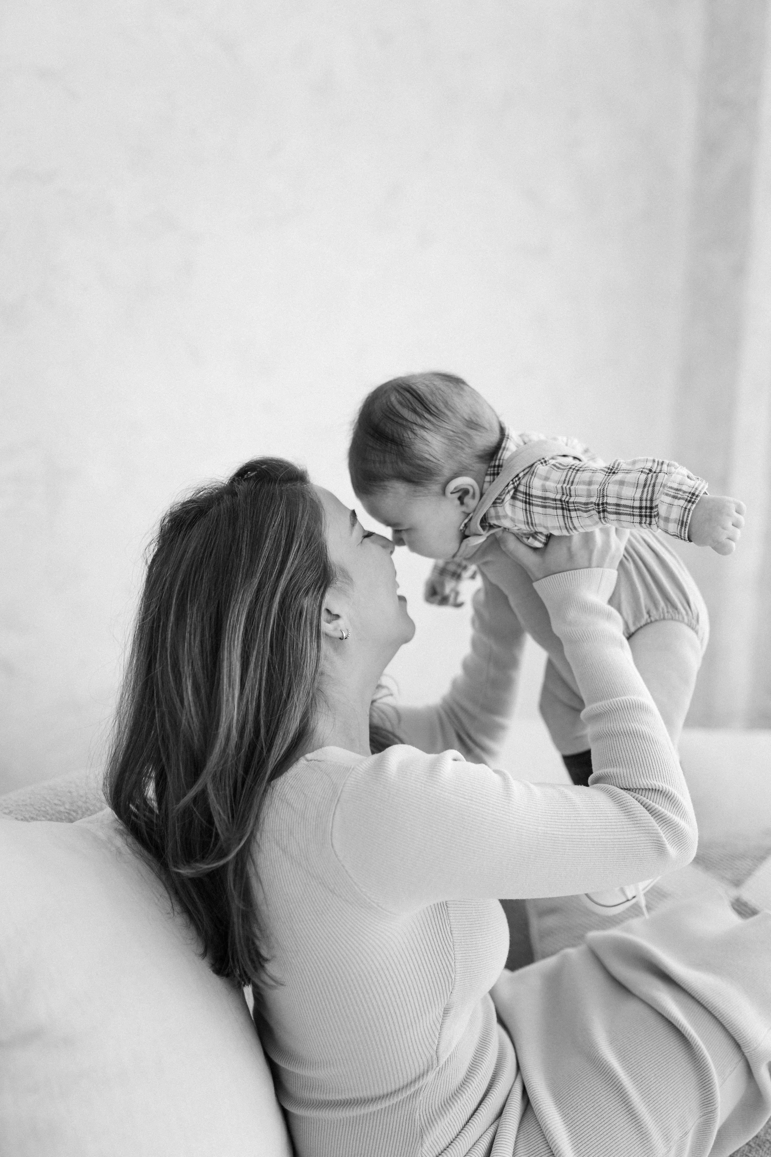A woman holding a young child close, touching their foreheads together in a tender moment indoors.