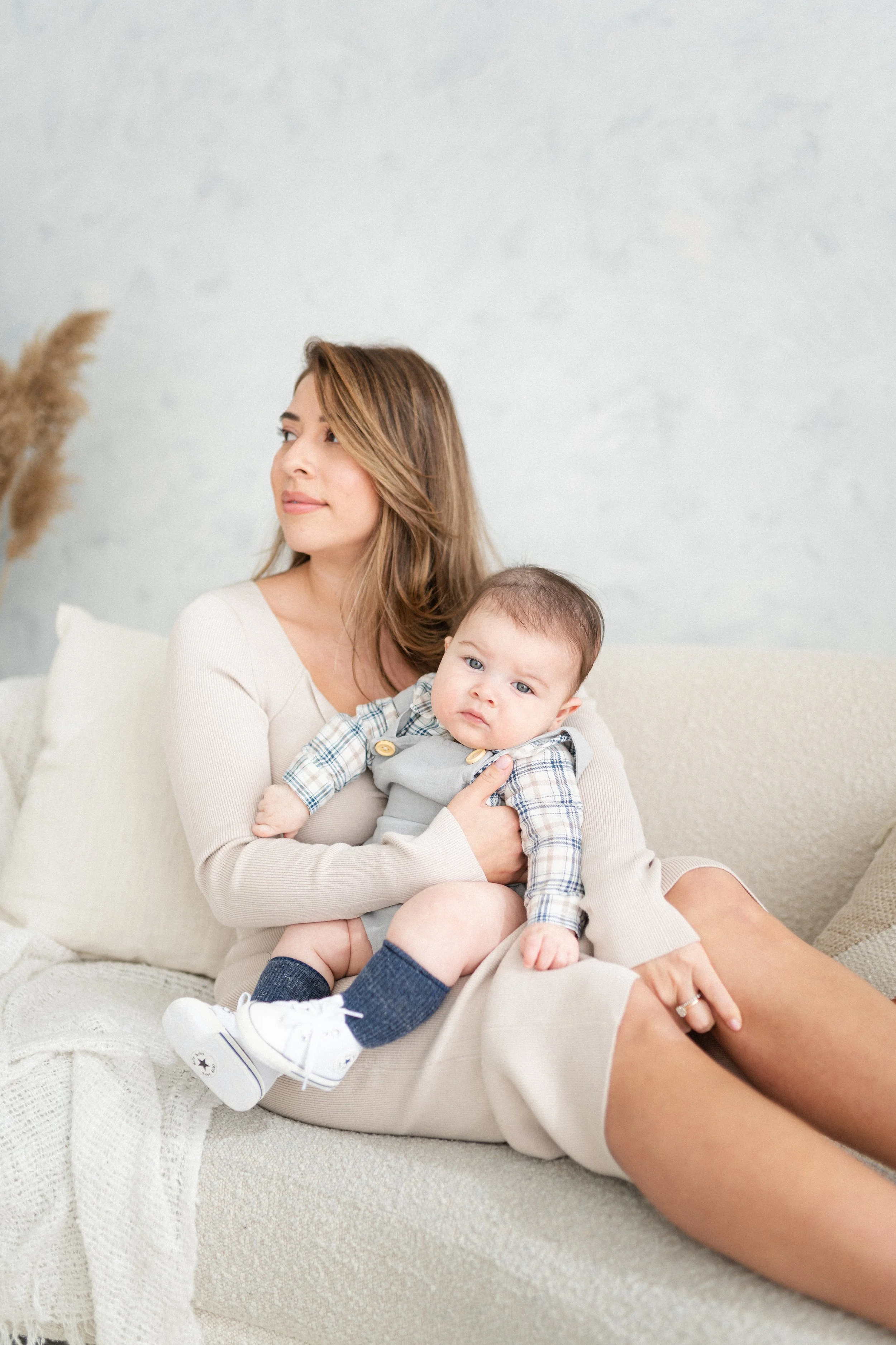 A woman sitting on a light-colored sofa holding a baby in her lap.