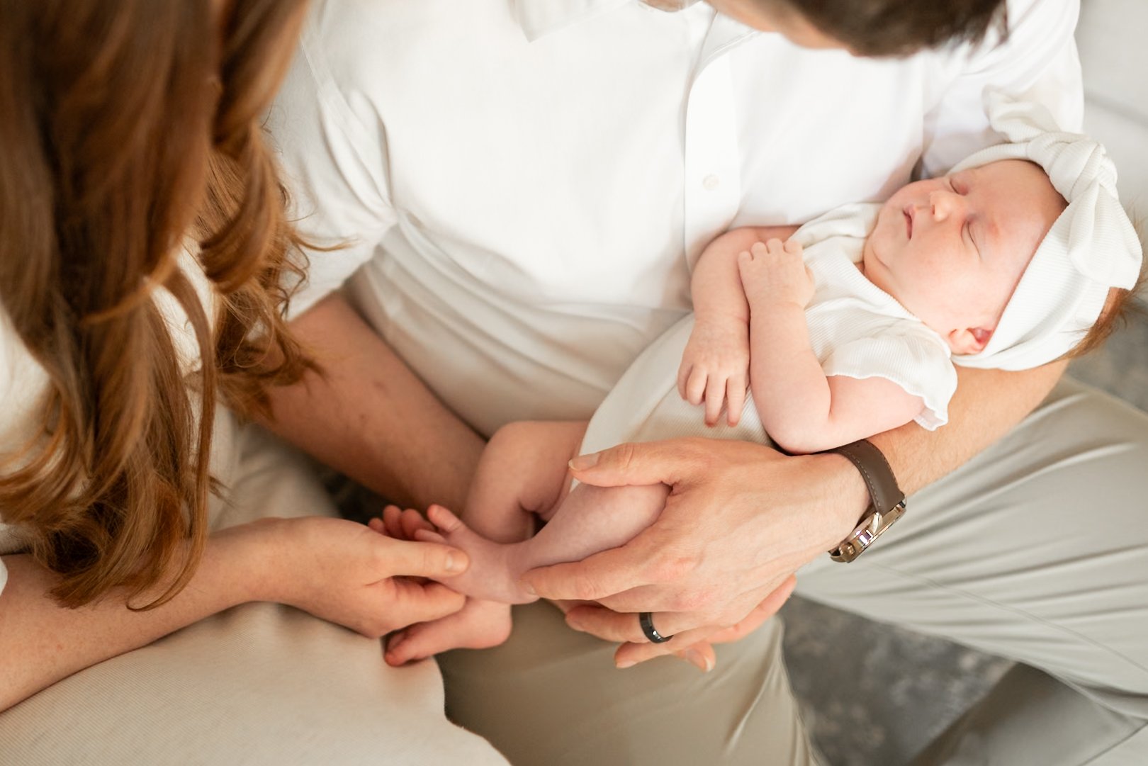 A newborn baby sleeping in the arms of a person, with another person gently holding the baby's foot.