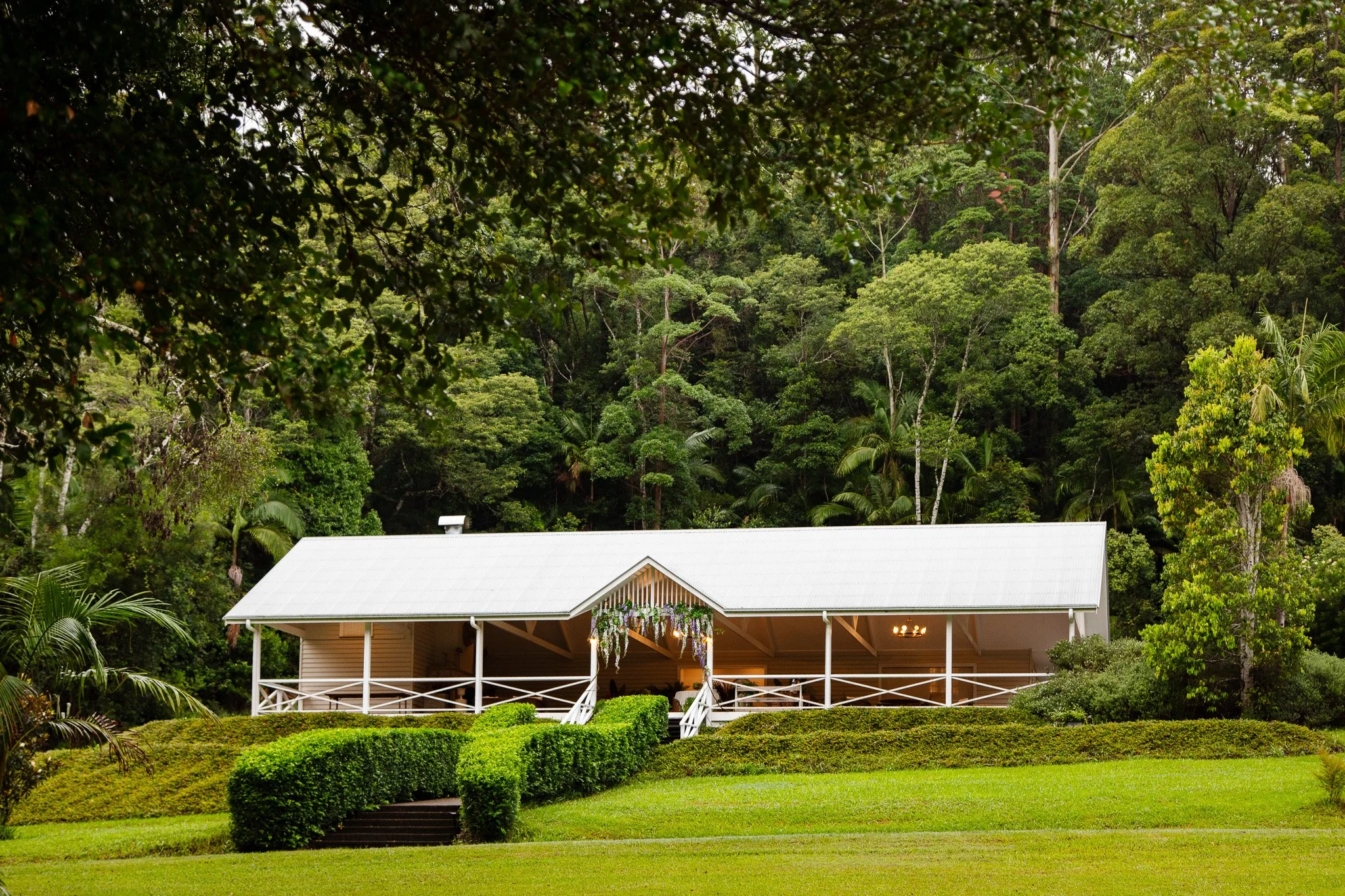 A white house with a green lawn and lush trees in the background.