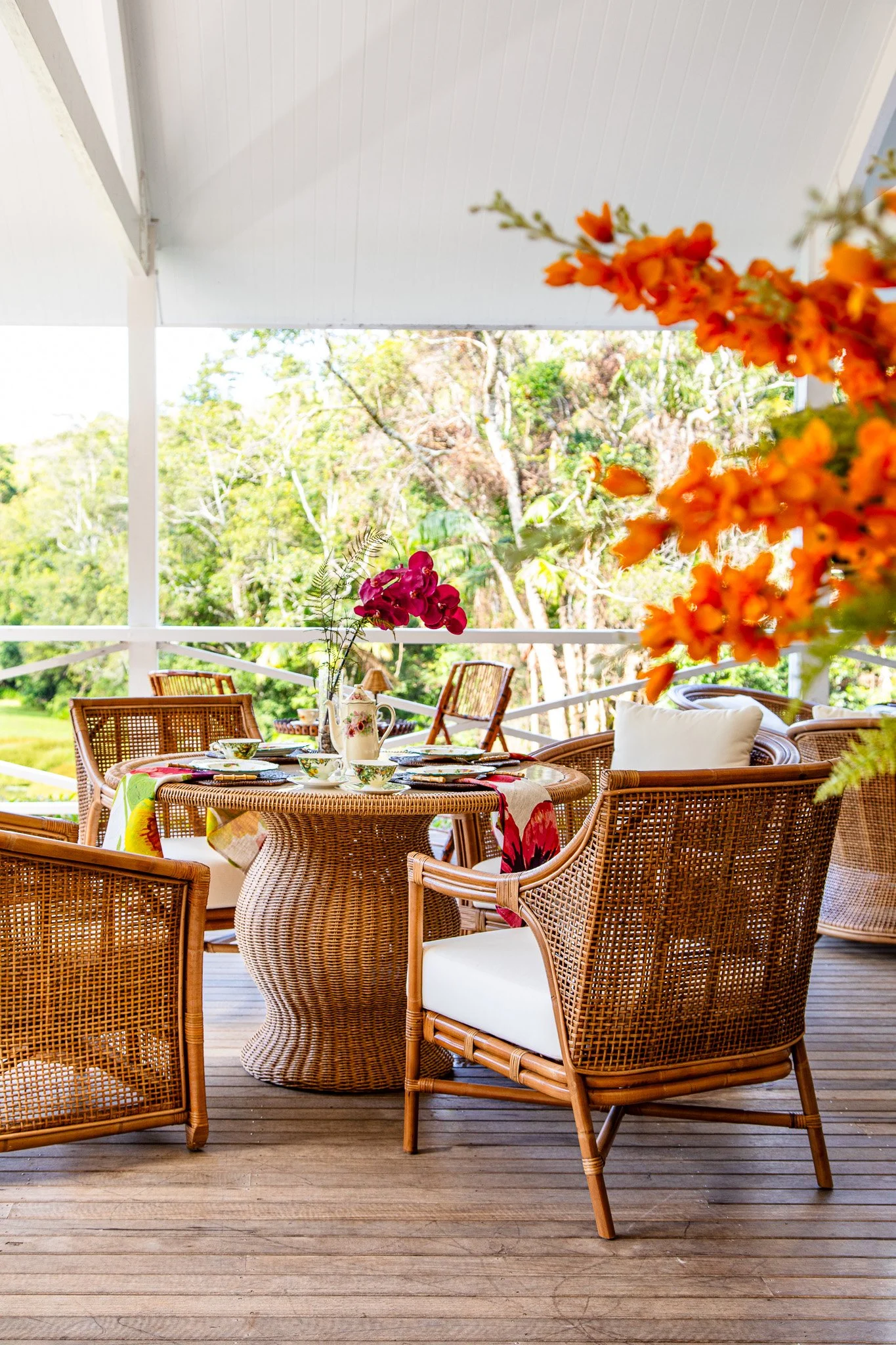A table setting inside The Palm Room at Nightcap Ridge ready for High Tea. There are flowers and cane chairs and a cane table
