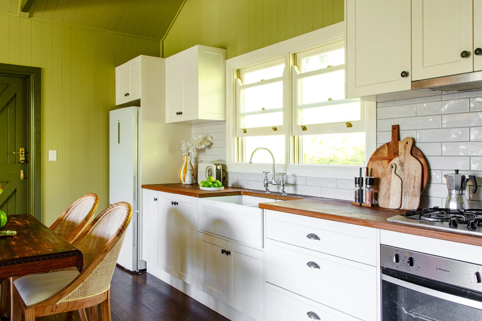 Kitchen with white cabinets, green walls, wooden countertops, window above sink, and dining table with chairs