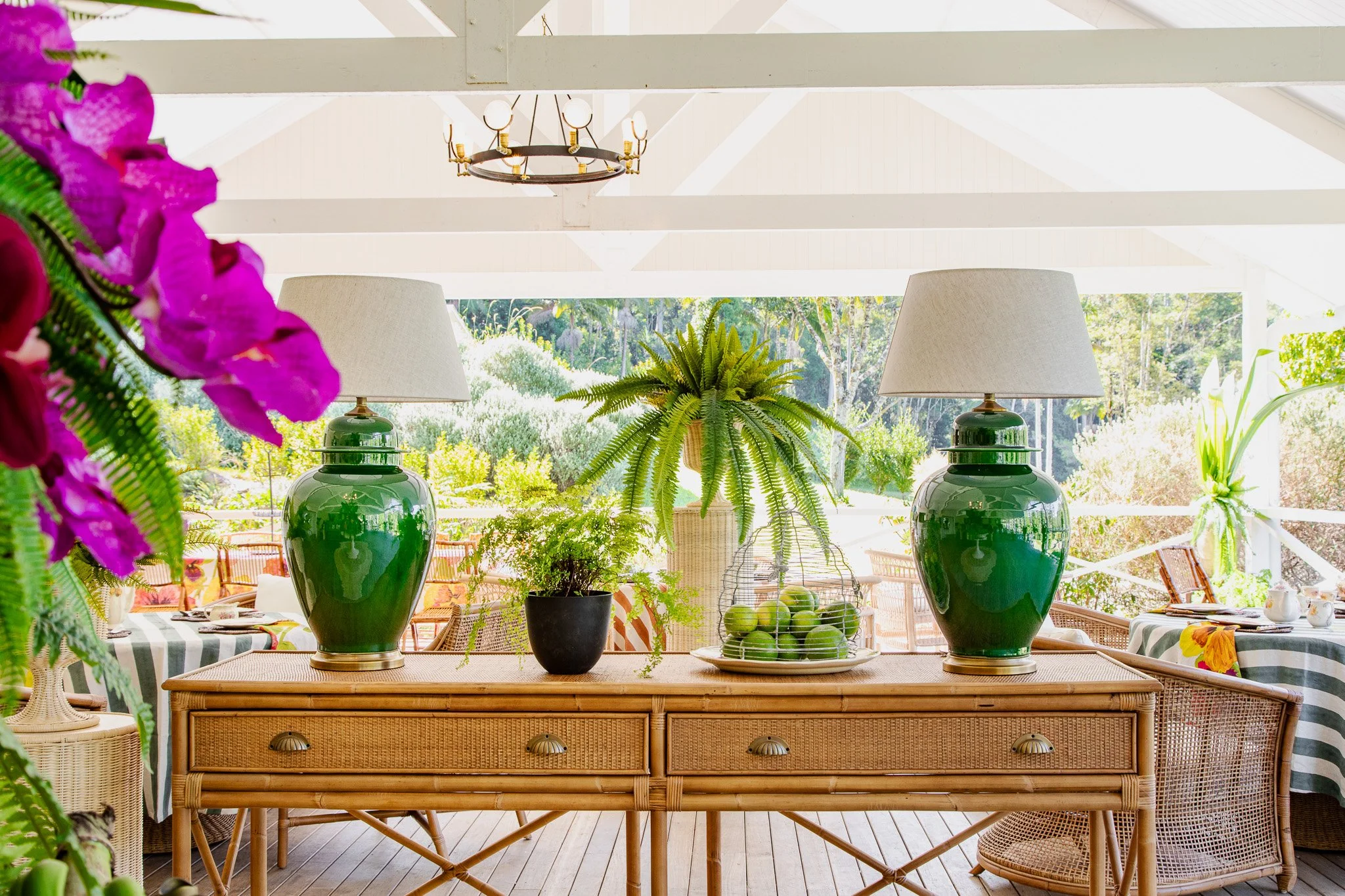 Decorative table with potted plants and green lamps in a bright sunlit patio or porch with outdoor scenery in the background.