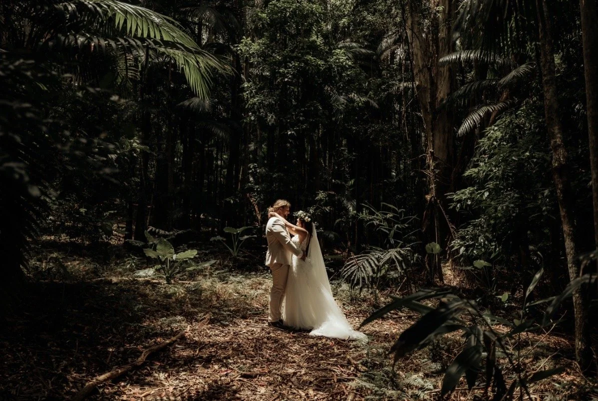 A bride and groom sharing a kiss in a dense jungle, surrounded by tall trees and lush green foliage.