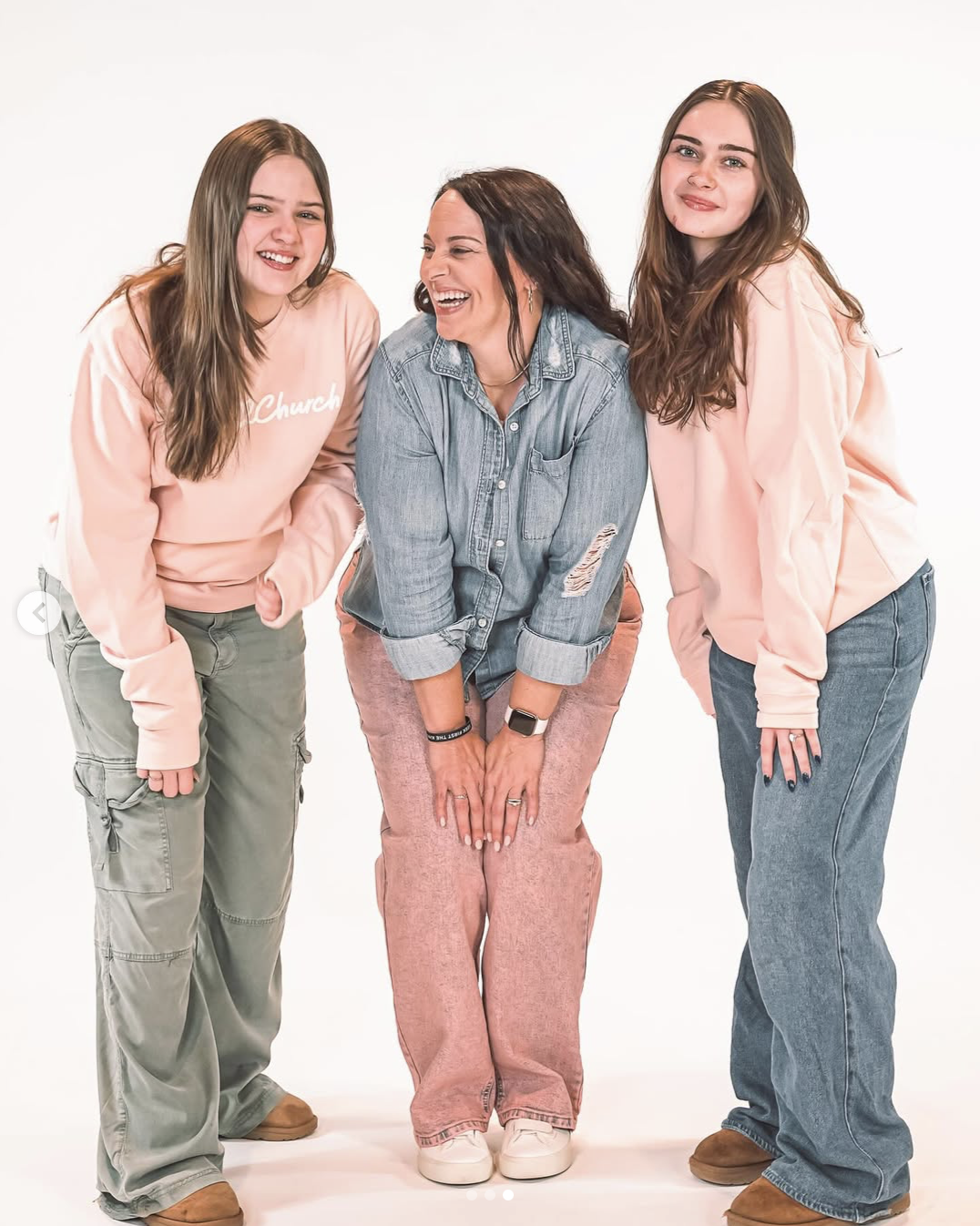 Photo of a mother and her two daughters laughing and posing in front of a white backdrop. Photo taken by Baylee Perry.