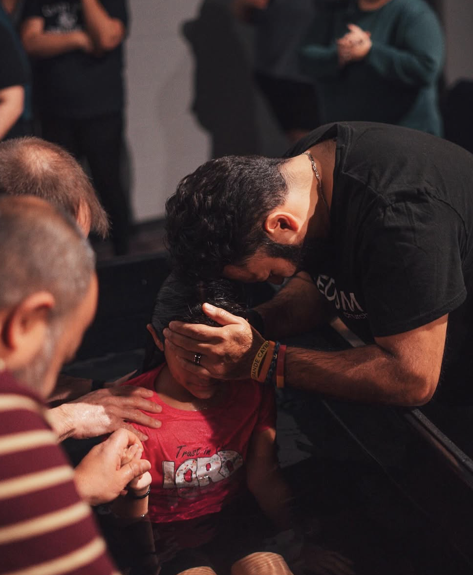 Photo of a man cupping his daughter's head during a baptism. Photo by Baylee Perry.