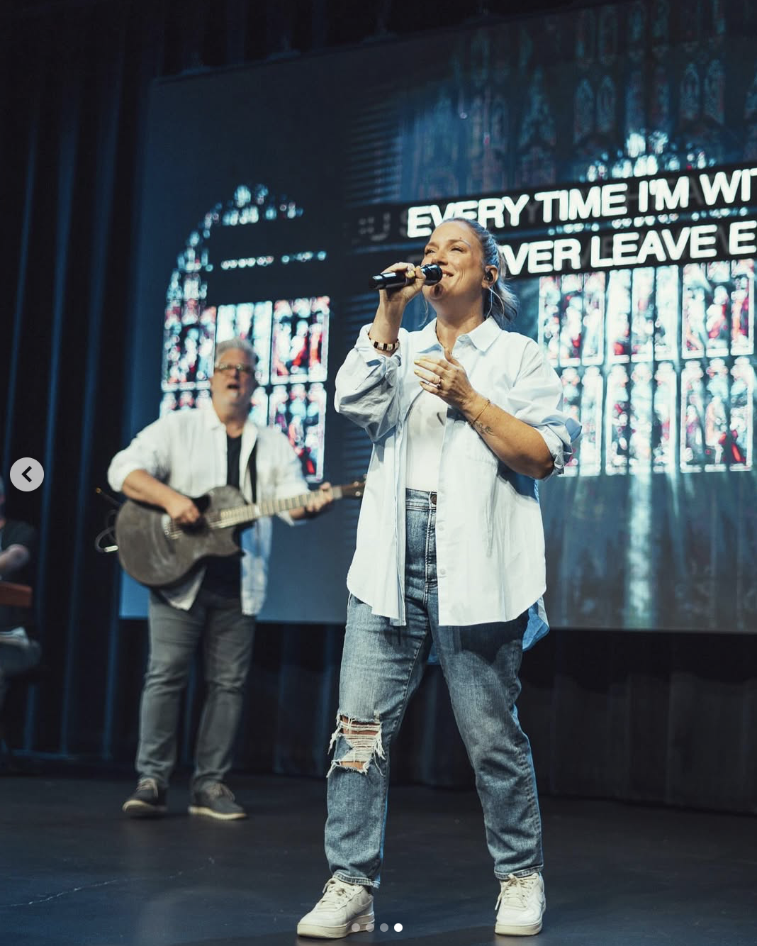 Photo of a woman singing on stage during a Sunday morning and a man behind her playing guitar. Photo by Baylee Perry.