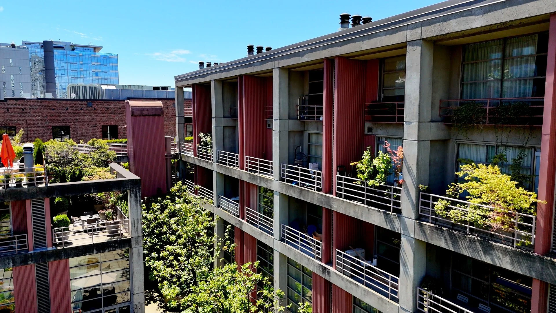 Multi-story apartment building with balconies decorated with greenery, trees, and outdoor furniture under a clear blue sky.