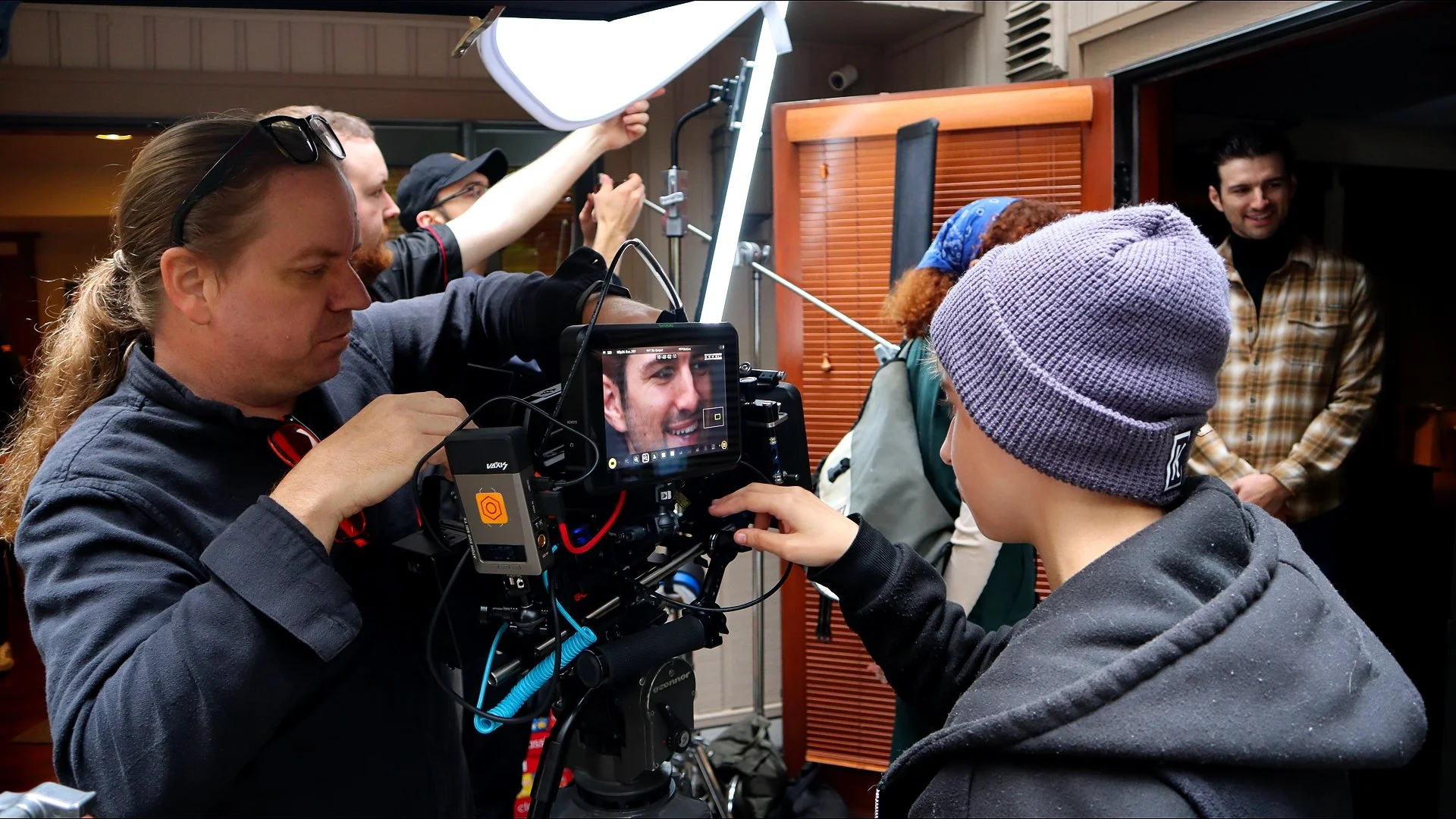 A film crew prepares a camera and monitors a young boy in a gray beanie, while two men and a woman stand in the background